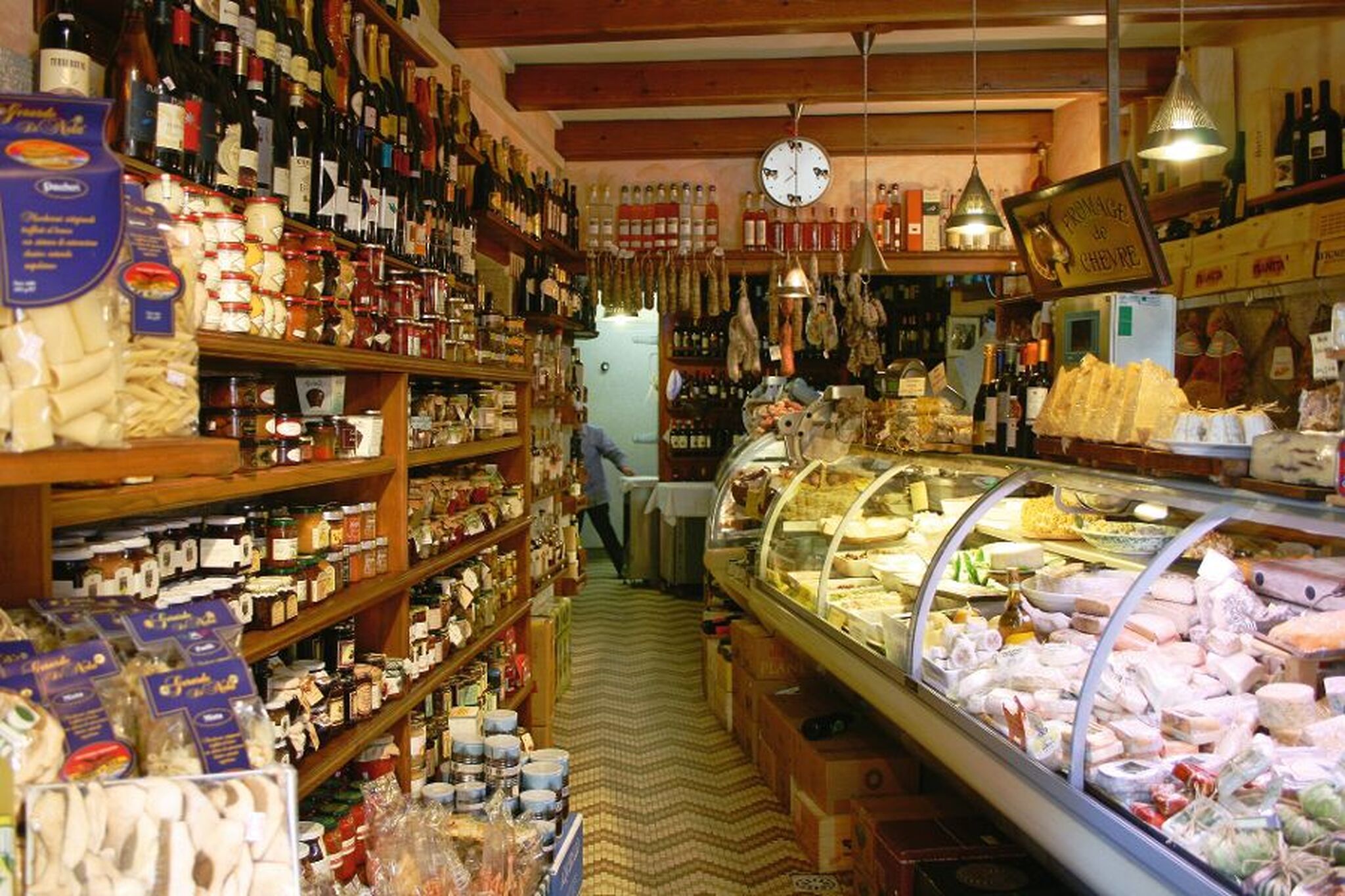 Innenansicht eines gut gefüllten Feinkostladens mit Regalen voller Produkte und einer Theke.