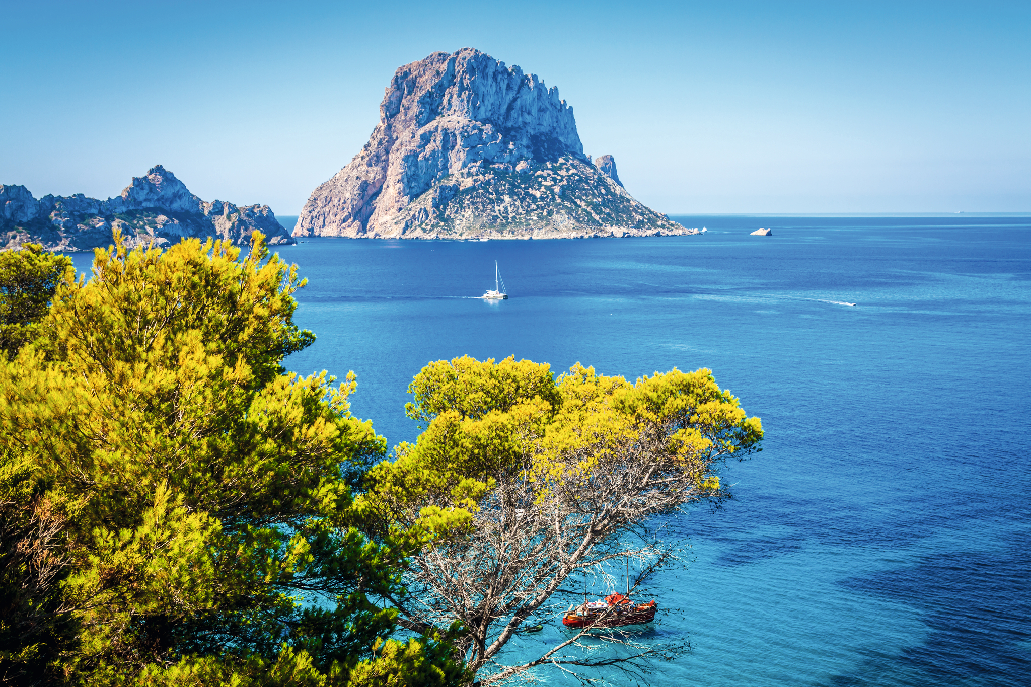 Blick von Cala d'Hort auf die Felseninsel Es Vedrà bei strahlend blauem Himmel und klarem Wasser.