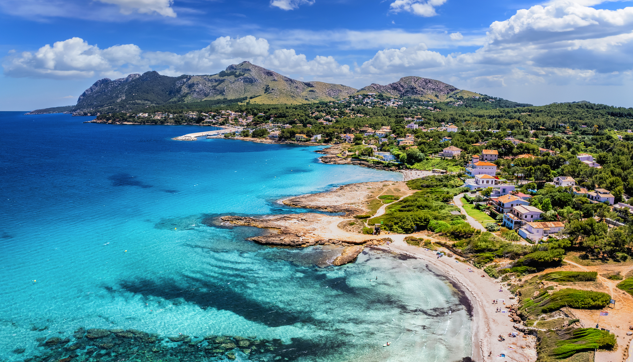 Küstenlandschaft mit blauem Meer, Sandstrand und Bergen im Hintergrund.