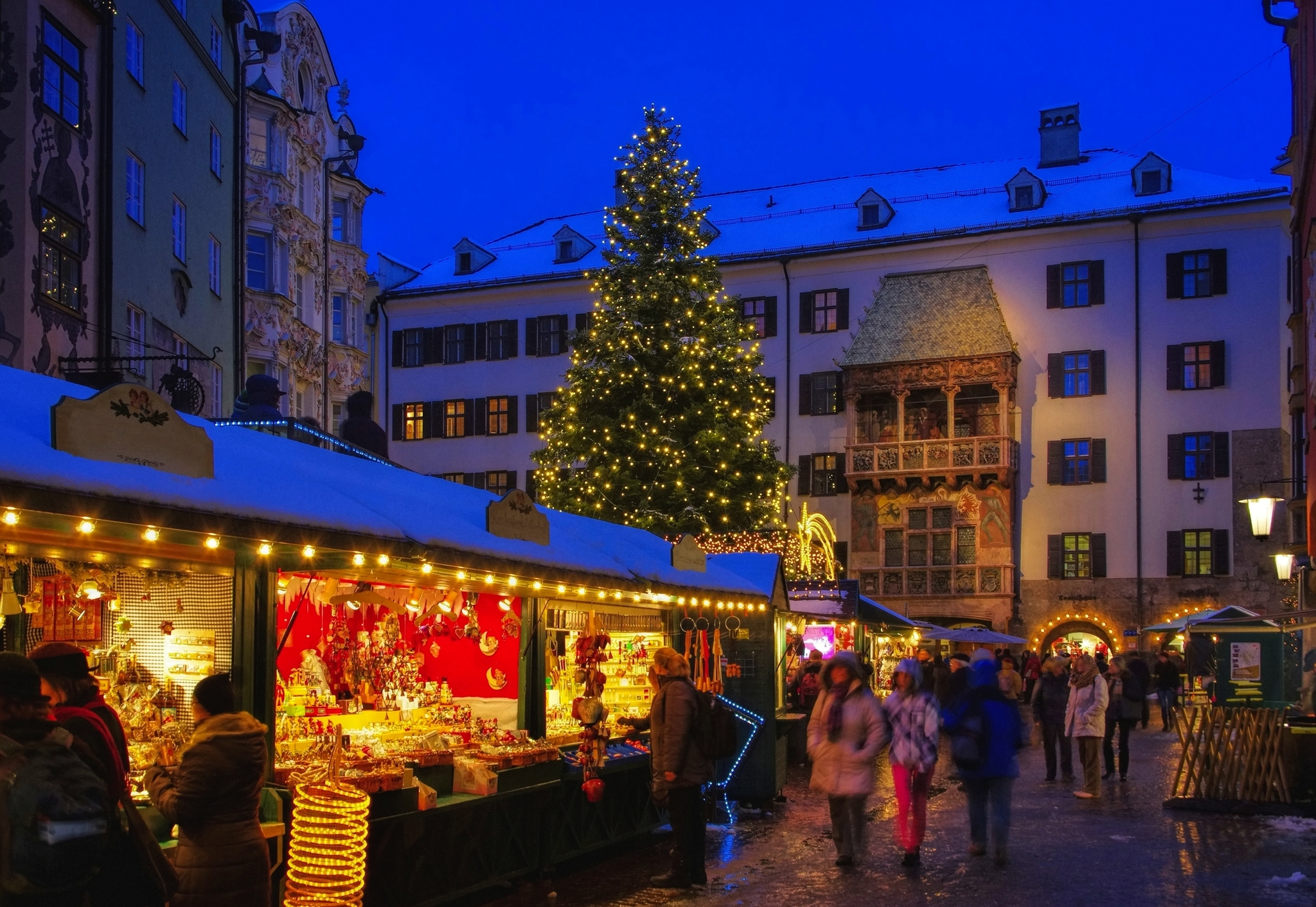 Weihnachtsmarkt mit festlich geschmücktem Baum und Ständen bei Abenddämmerung.