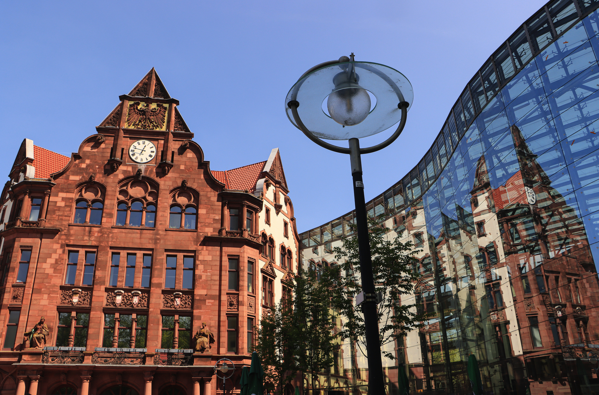 Historisches Gebäude mit Uhr neben moderner Glasfassade und Straßenlaterne.