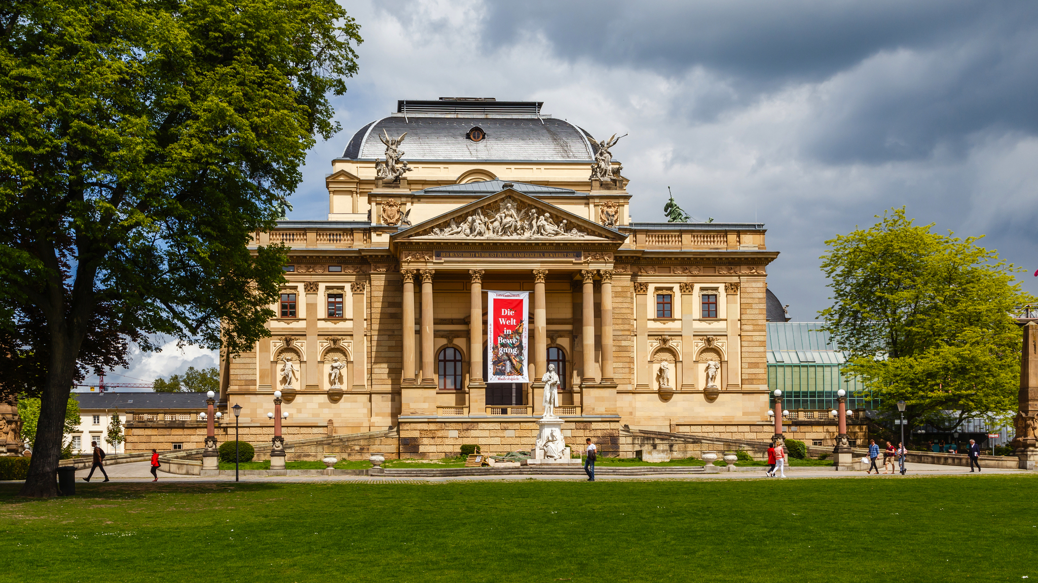 Hessisches Staatstheater Wiesbaden mit beeindruckender neoklassizistischer Architektur, umgeben von Bäumen und besucherfreundlichem Vorplatz.