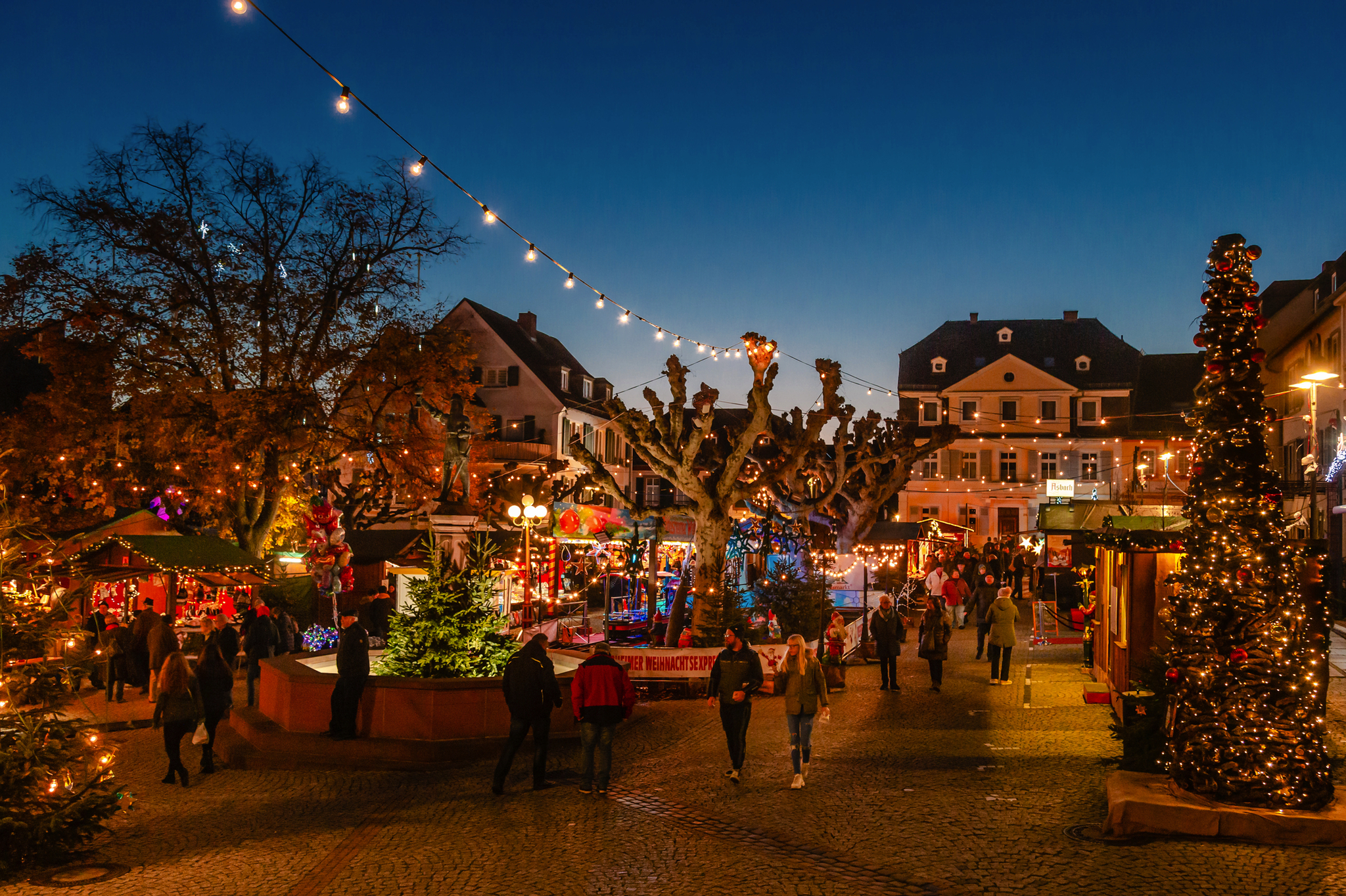 Weihnachtsmarkt mit Lichtern, Buden und Menschen bei Abenddämmerung.