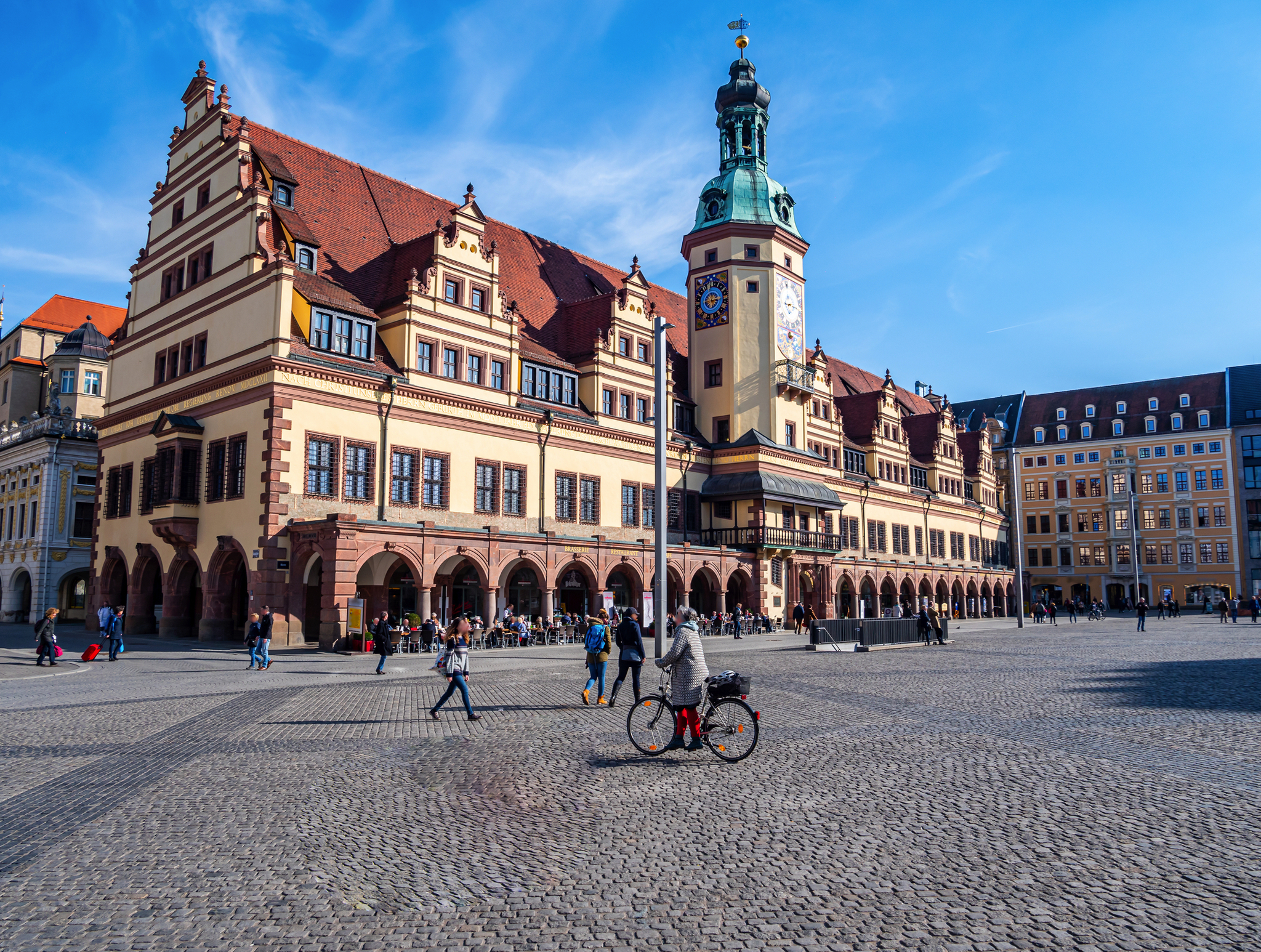 Historisches Gebäude mit Turm auf großem, belebtem Platz bei blauem Himmel.