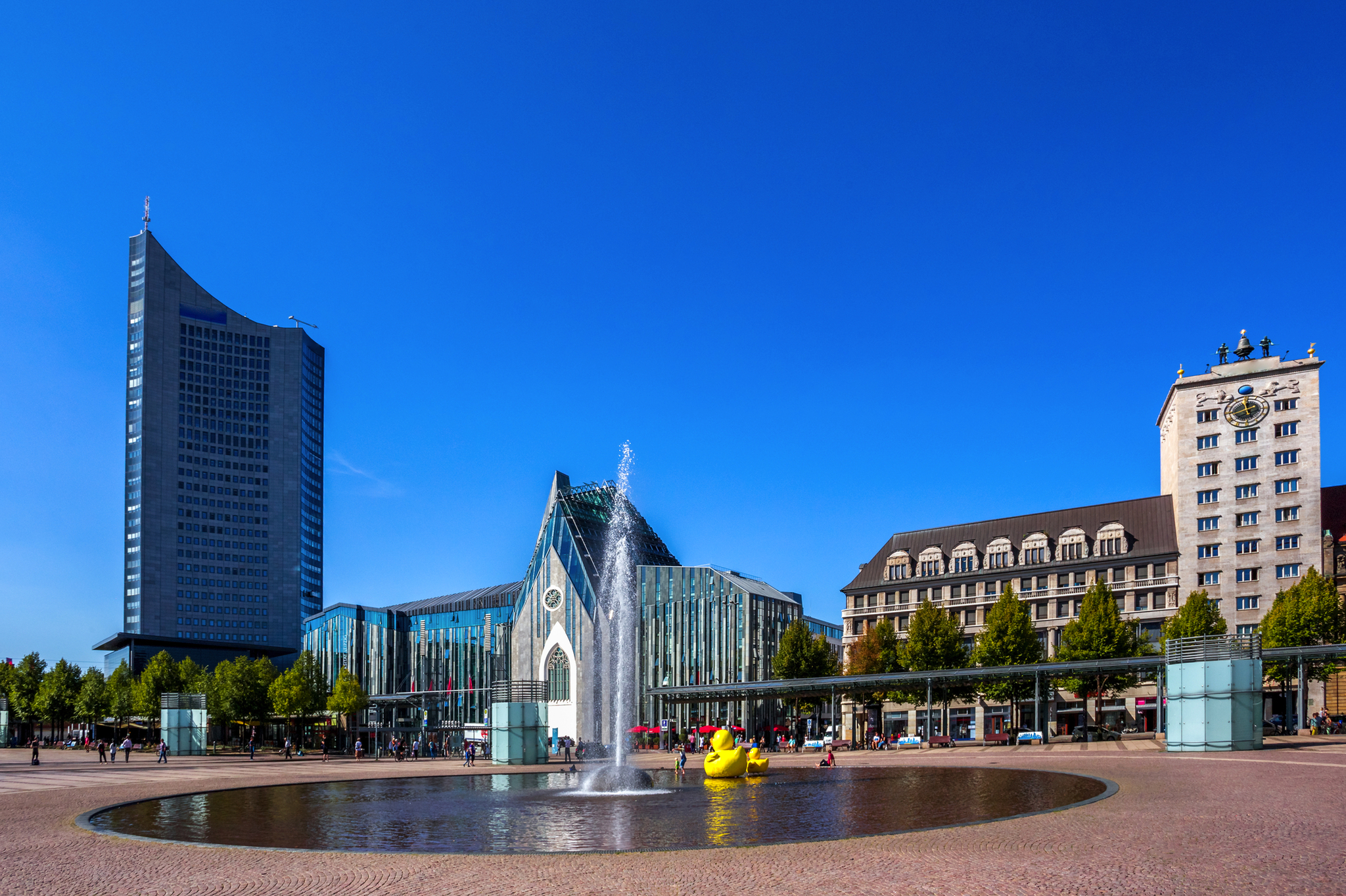 Springbrunnen und Gebäude am Augustusplatz in Leipzig bei klarem Himmel.