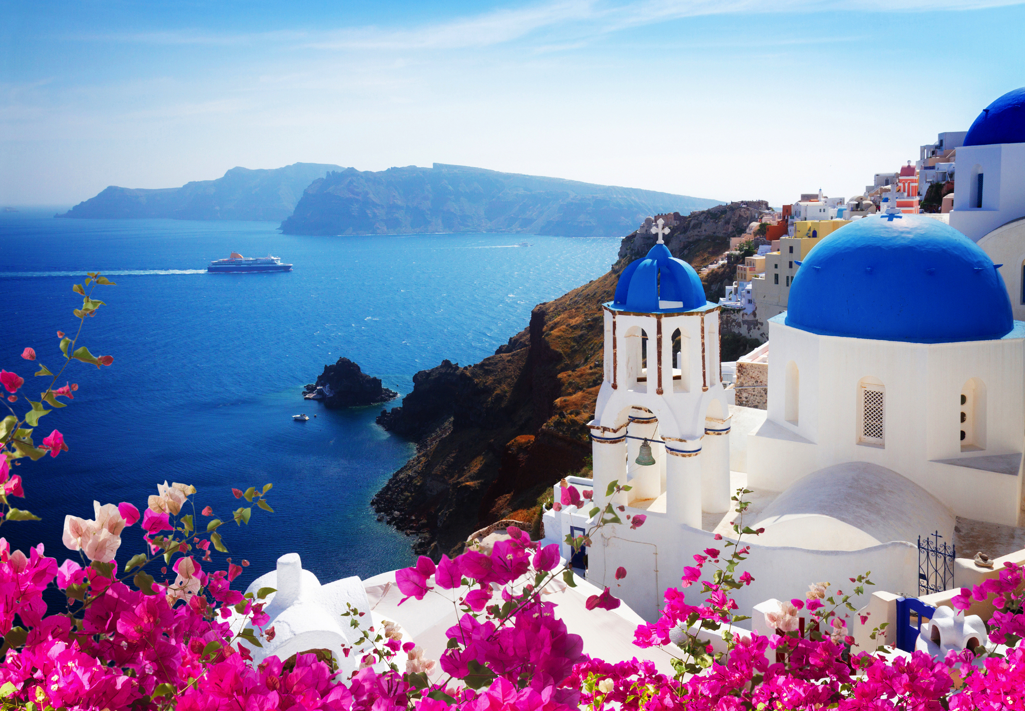 Blick auf Santorin mit blauem Meer, weißen Gebäuden und blühenden Bougainvillea.