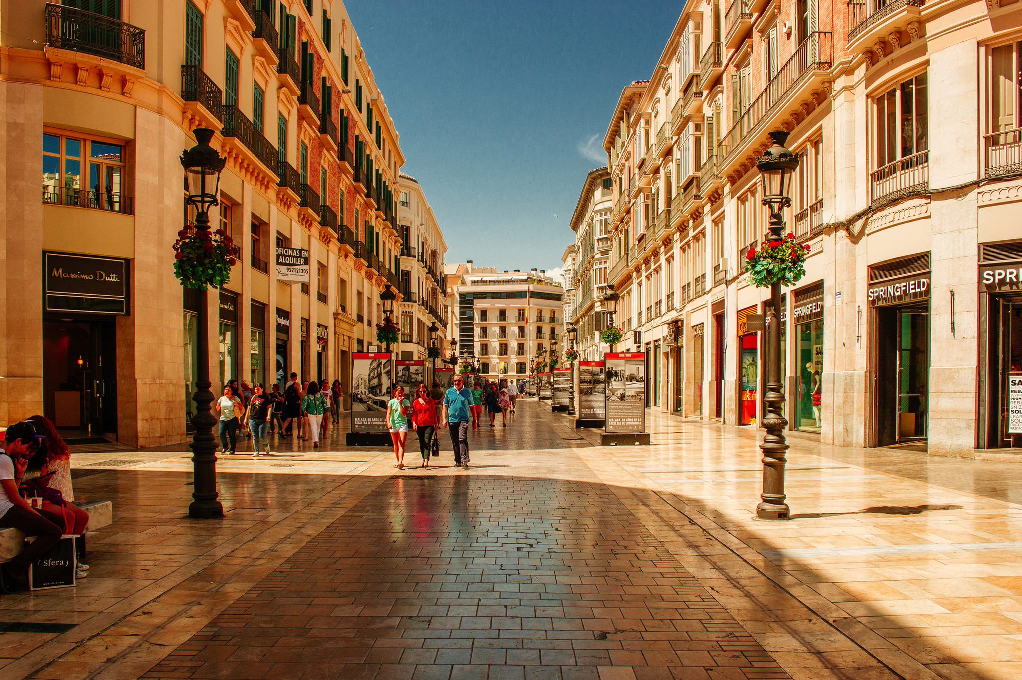 Einkaufsstraße in mediterraner Stadt bei sonnigem Wetter.
