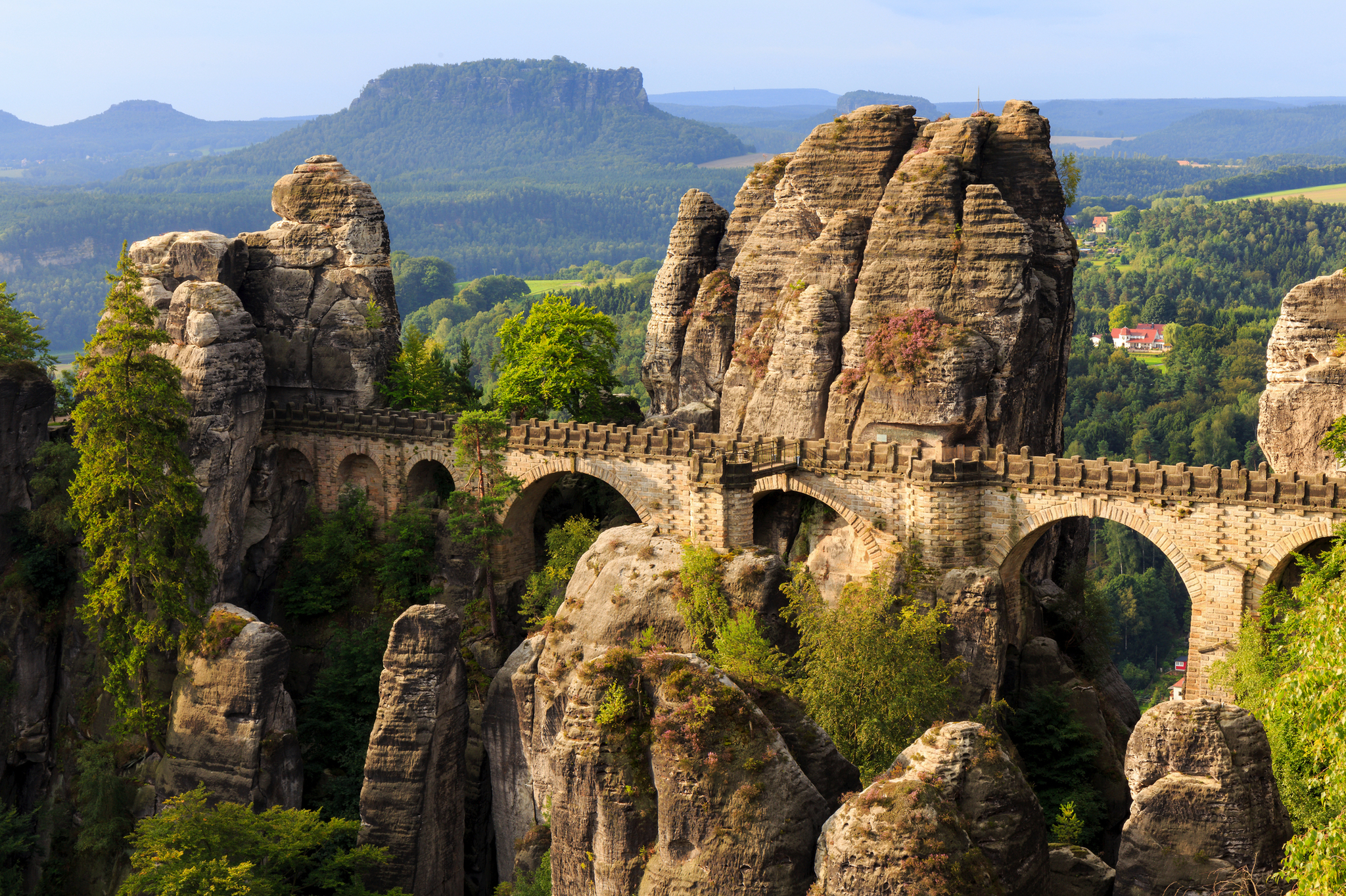Eine steinerne Brücke zwischen Felsformationen in einer bewaldeten Landschaft.