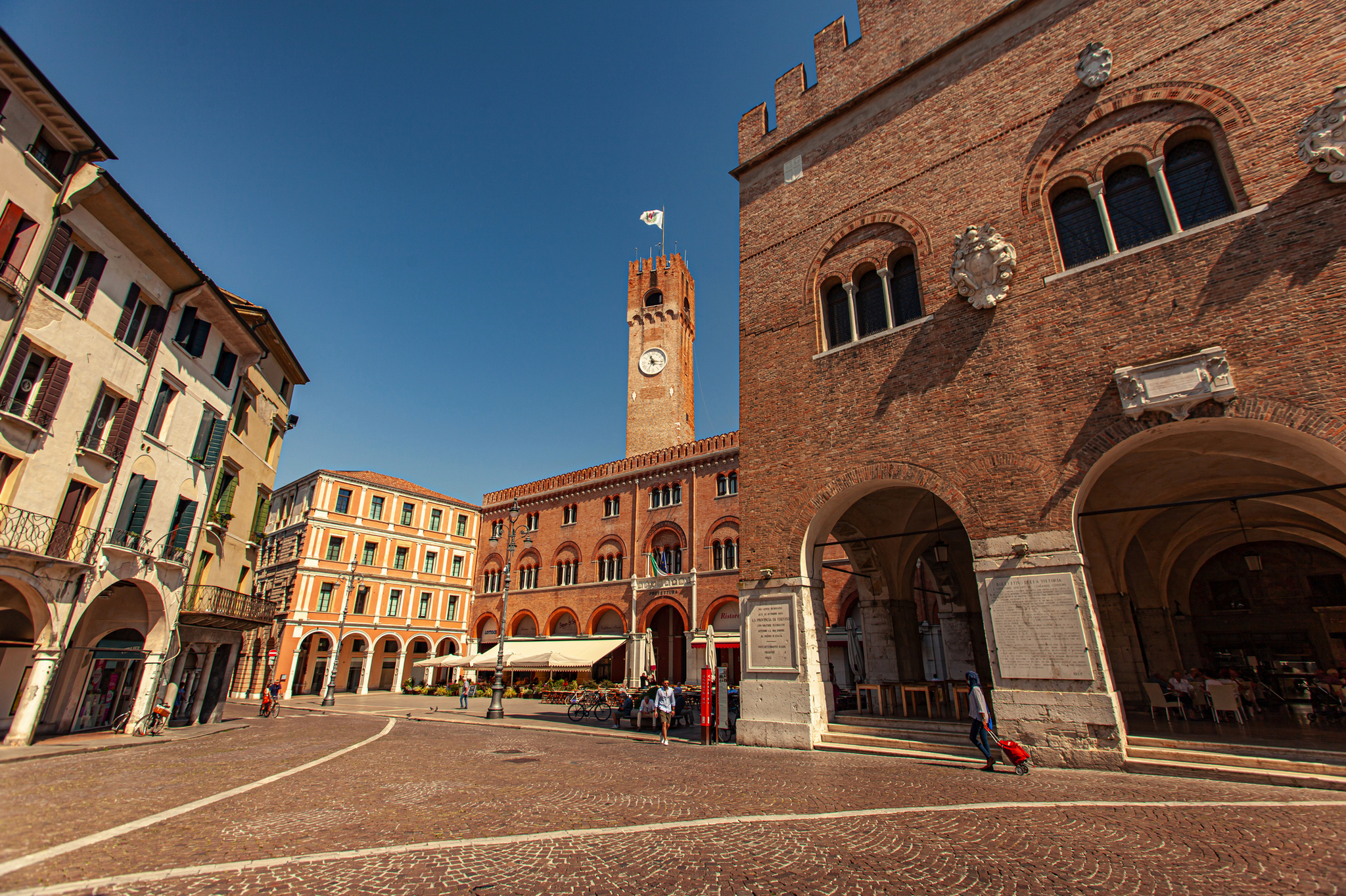Piazza dei Signori in Treviso mit historischen Gebäuden und Uhrturm bei sonnigem Wetter.