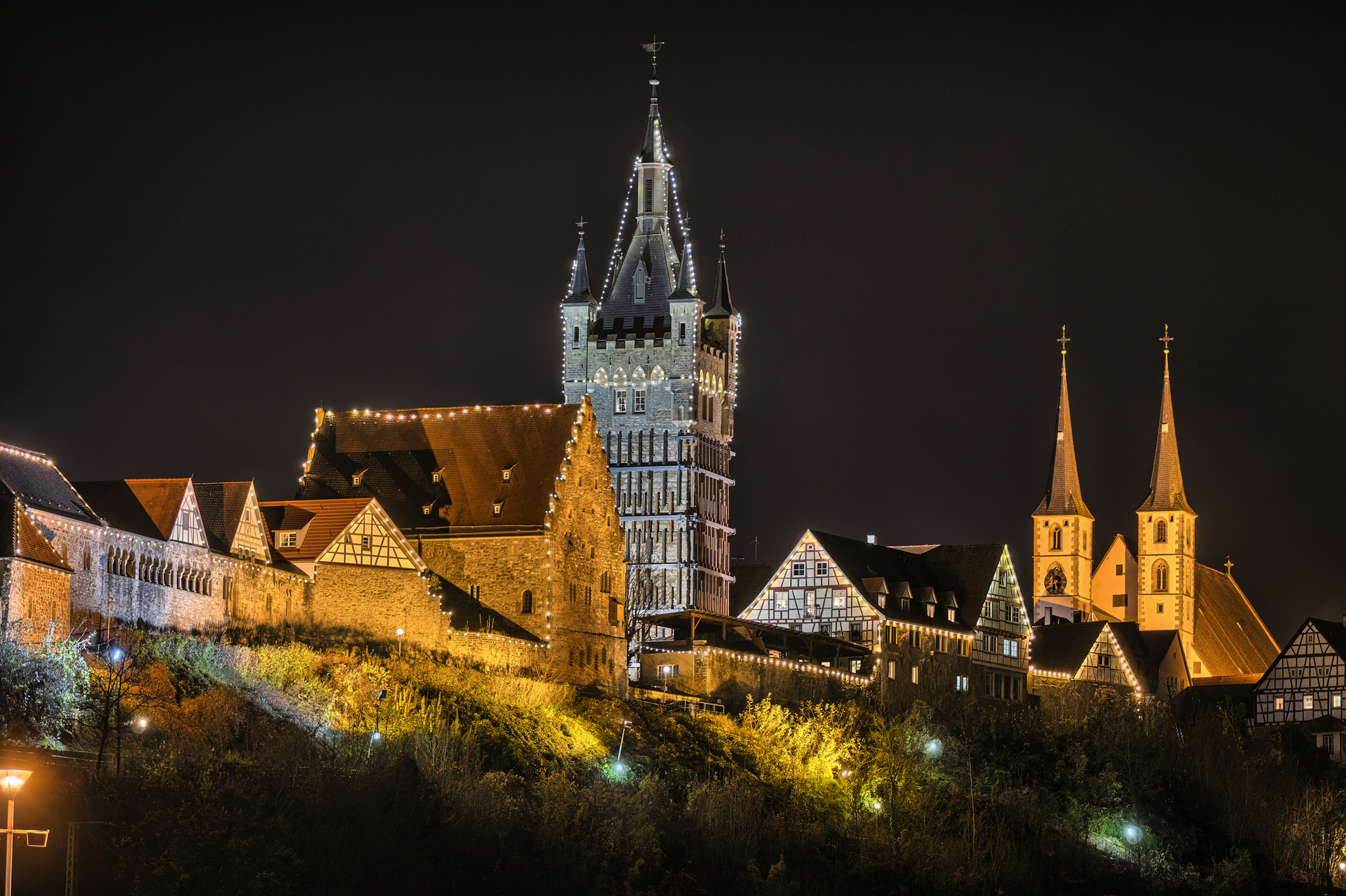 Beleuchteter Schlosskomplex bei Nacht mit Türmen und Fachwerkhäusern.