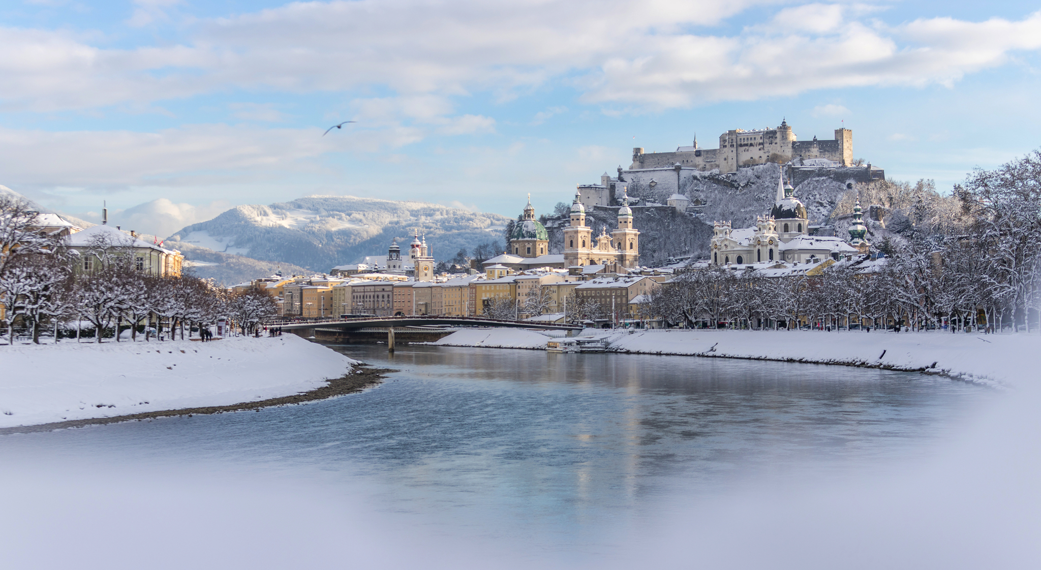 Winterliche Stadtlandschaft mit Fluss und Burg im Hintergrund.