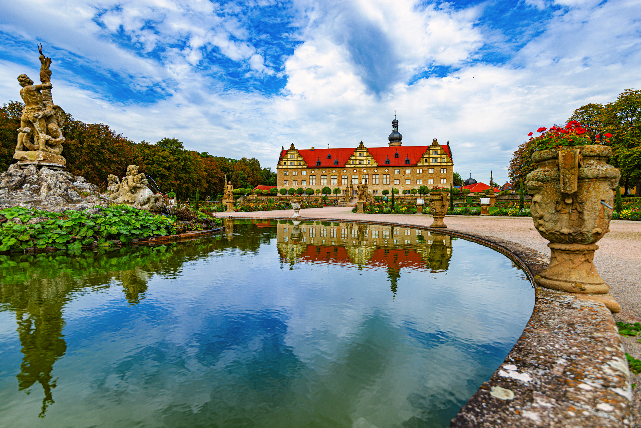 Schloss mit rotem Dach und Teich im Vordergrund an einem bewölkten Tag.