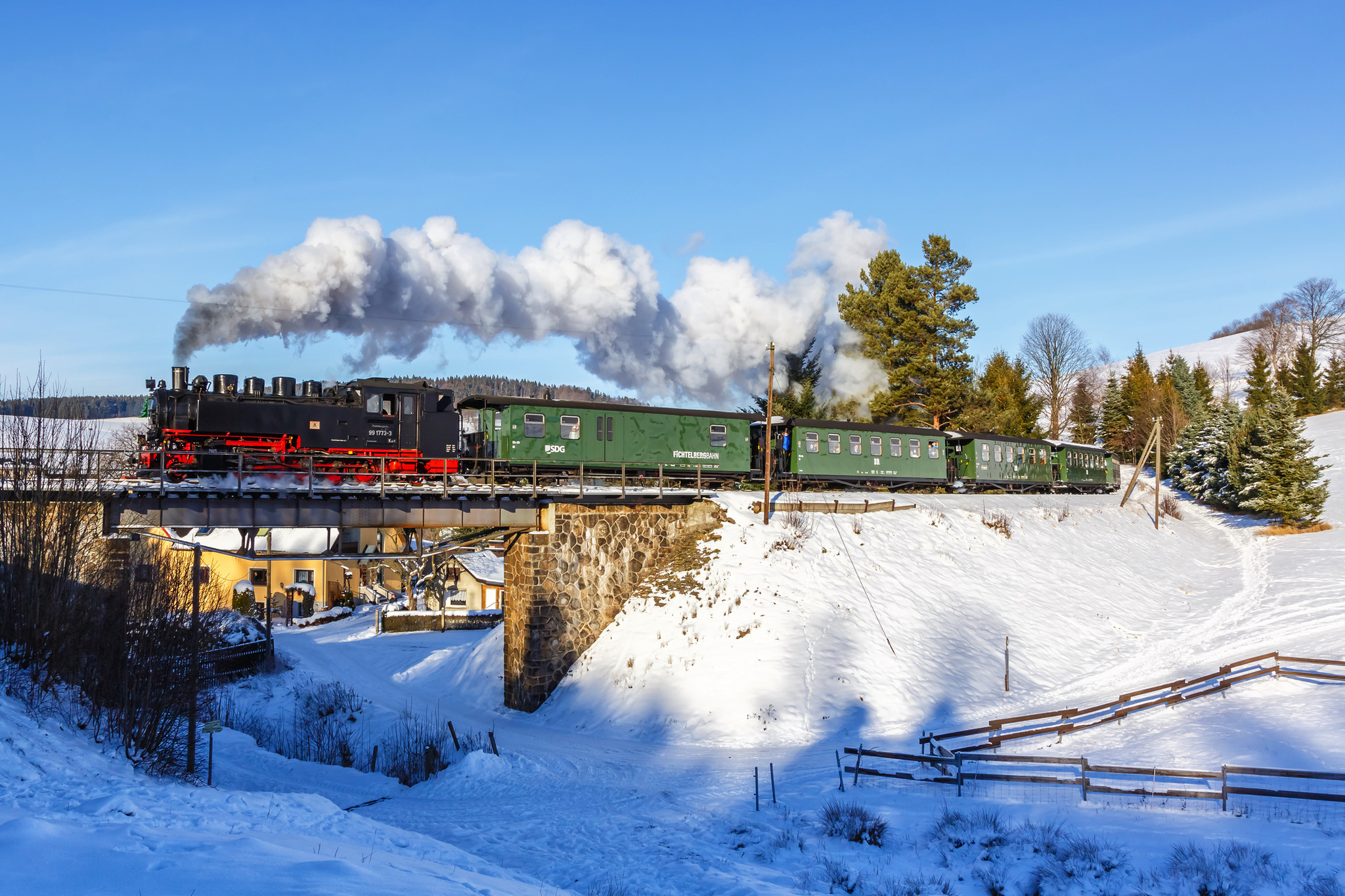 Schwarze Dampflok auf Brücke in verschneiter Winterlandschaft.