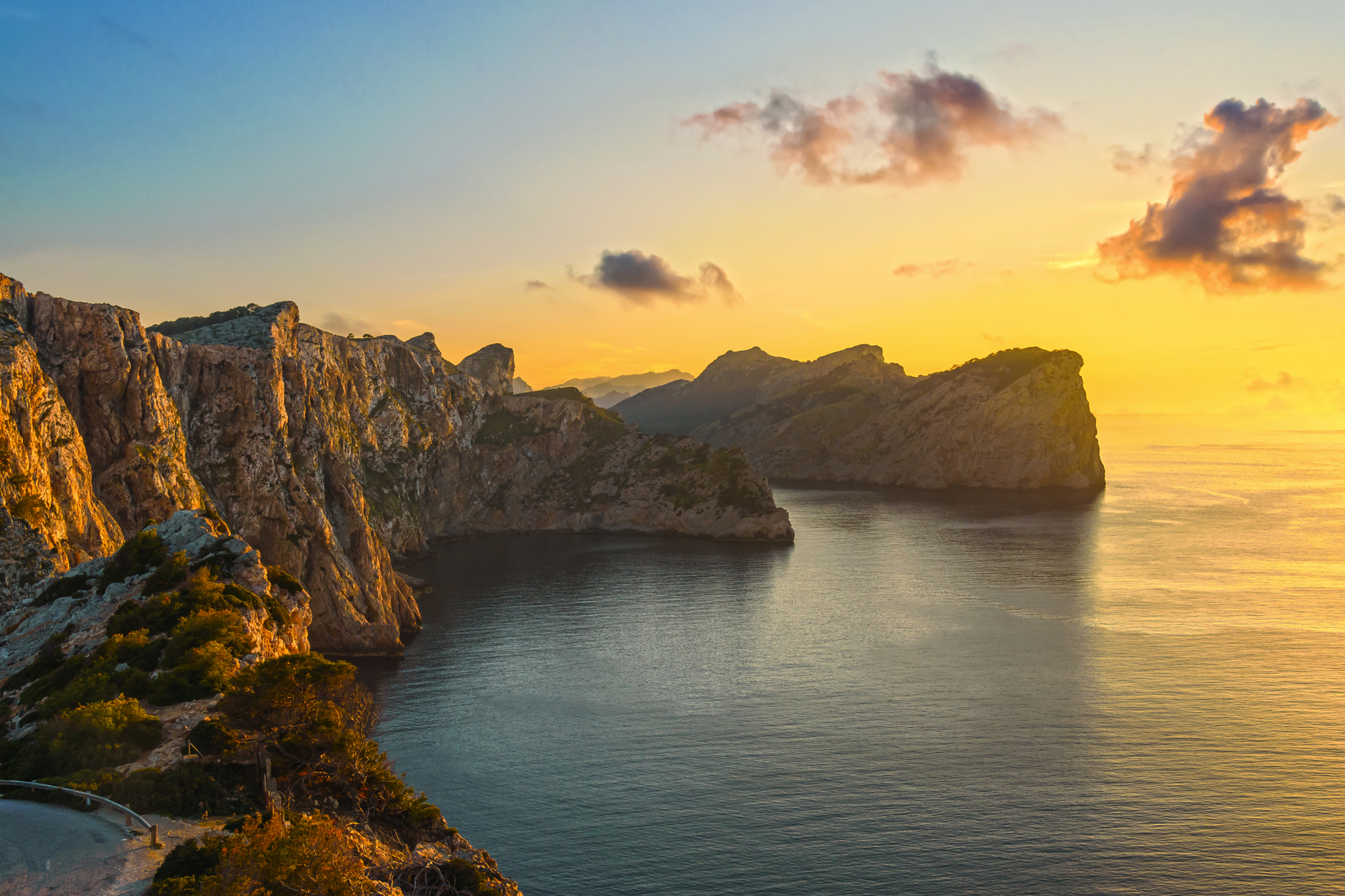 Klippenlandschaft bei Sonnenuntergang mit ruhigem Meer und Wolken am Himmel.