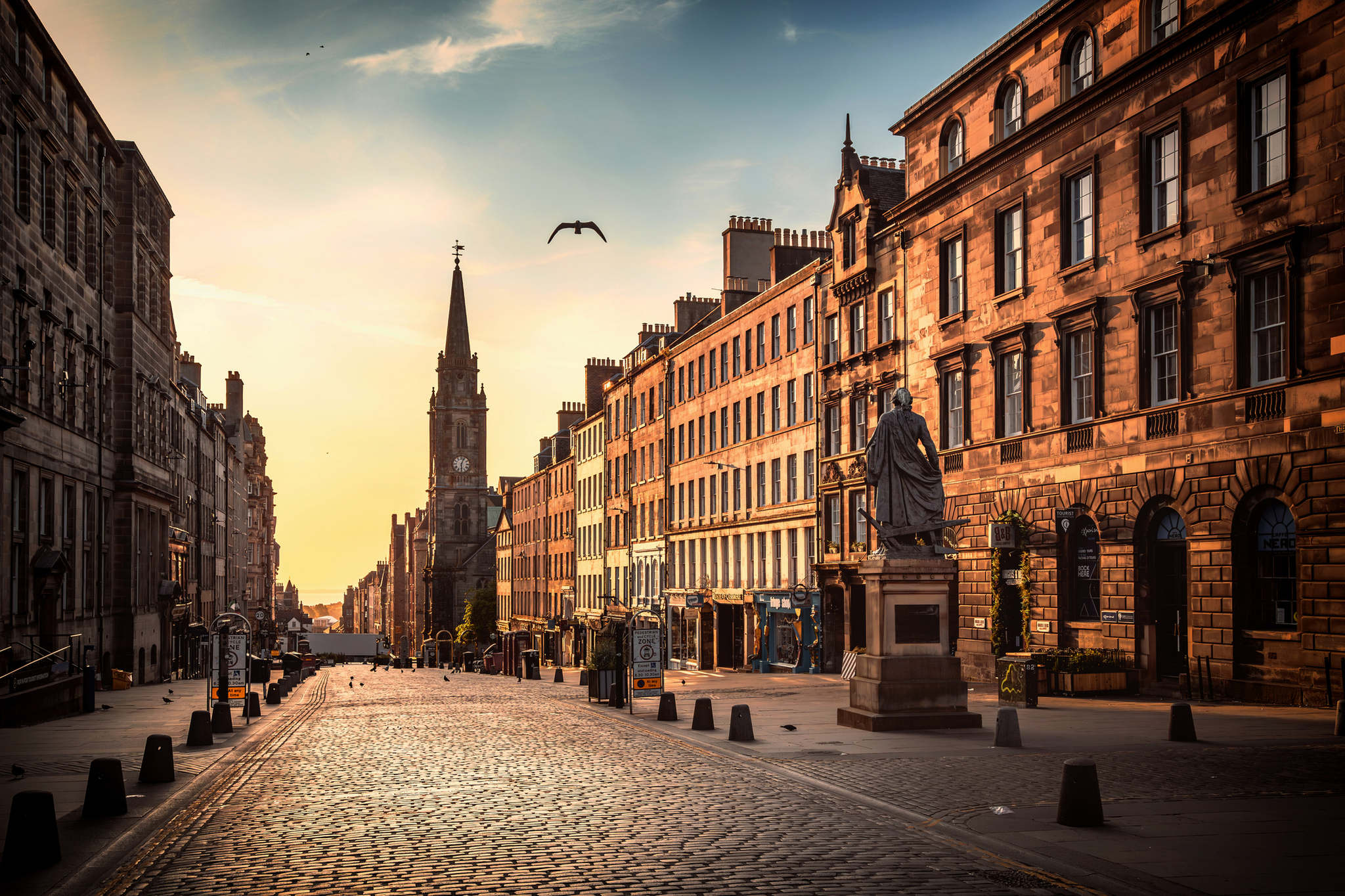 Straße mit Kopfsteinpflaster, historischen Gebäuden und einer Kirche im Hintergrund bei Sonnenuntergang.
