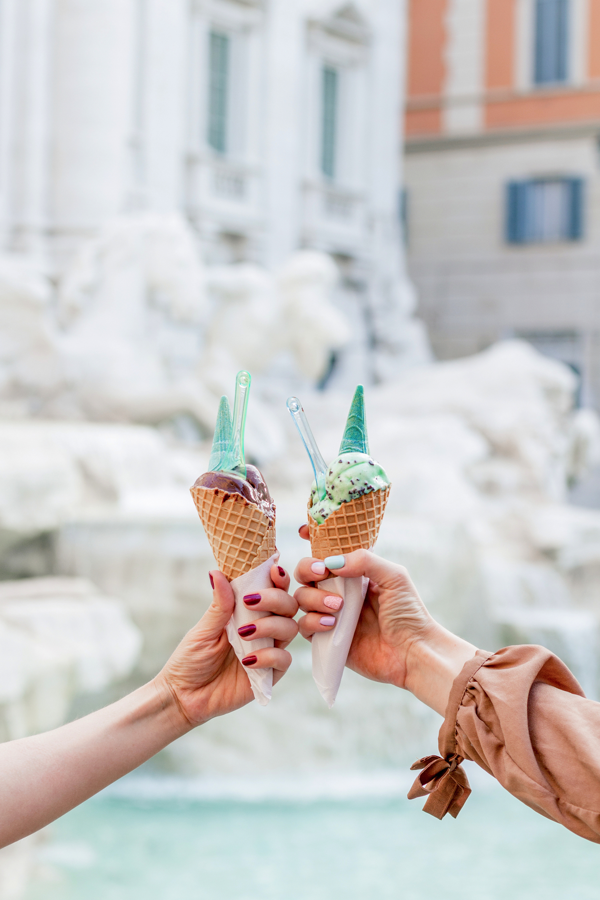 Zwei Personen halten Eistüten vor einem Brunnen hoch.