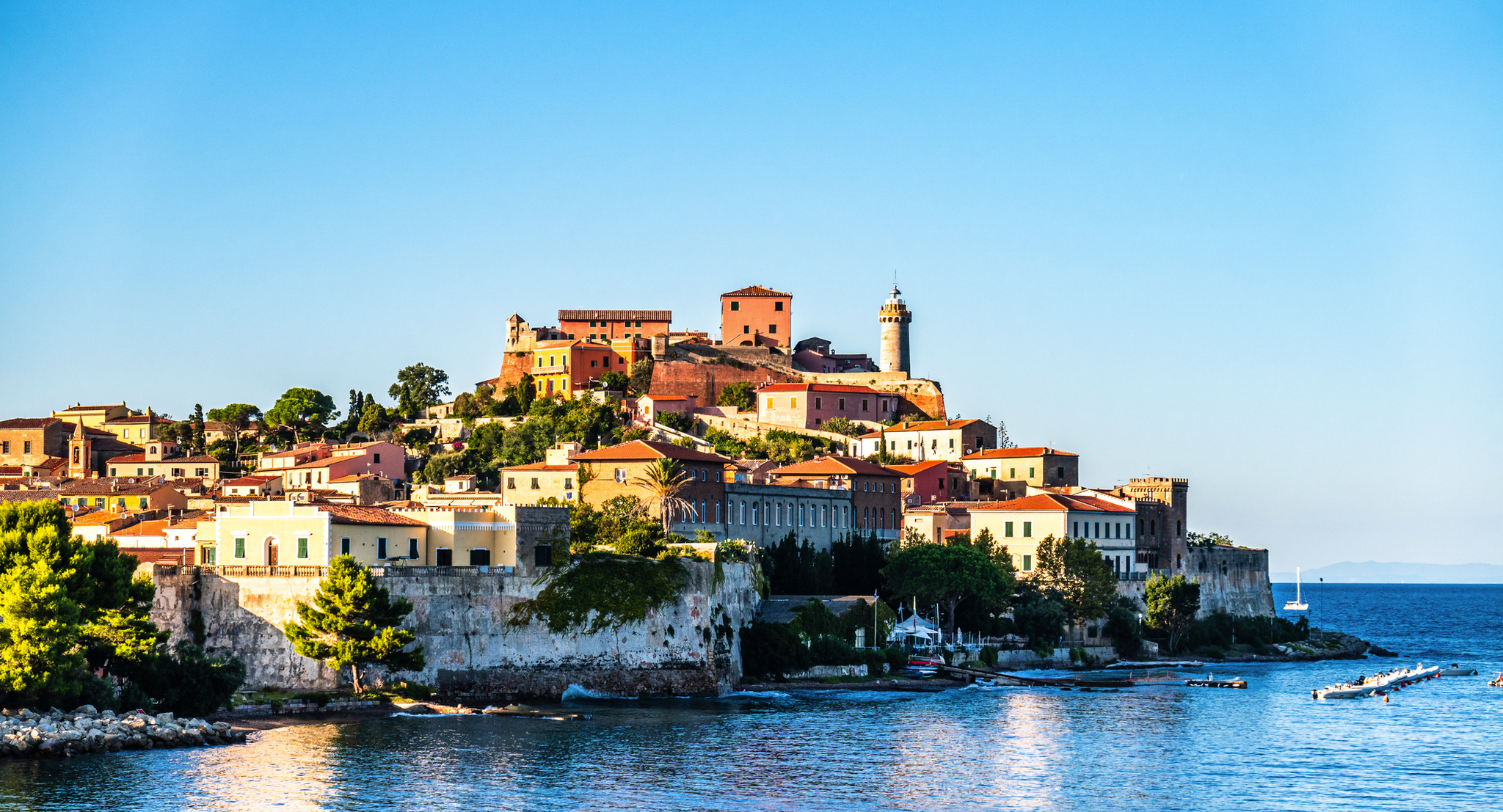 Hafen von Portoferraio auf der Insel Elba in Italien, mit bunten Gebäuden und einem Leuchtturm bei klarem Himmel.