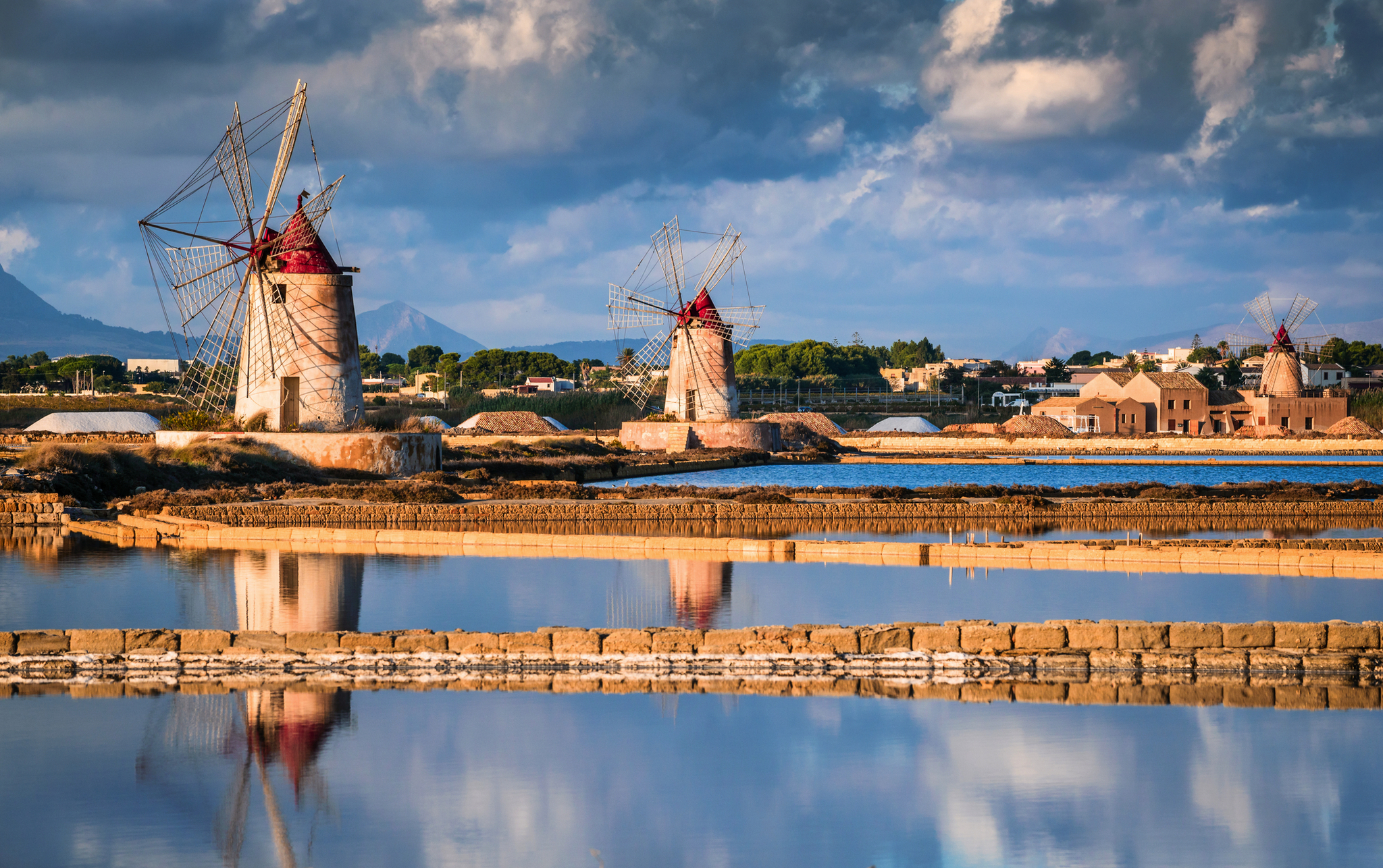 Windmühlen in den Salinen von Marsala, Sizilien, umgeben von Wasserflächen und Salzlagern.