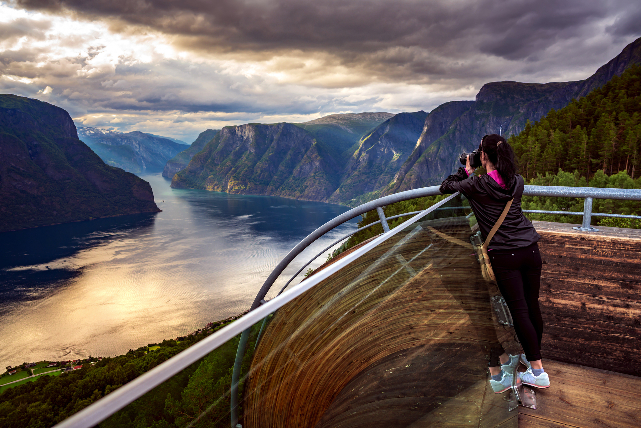 Person fotografiert Landschaft von Aussichtspunkt mit Fjord und Bergen im Hintergrund