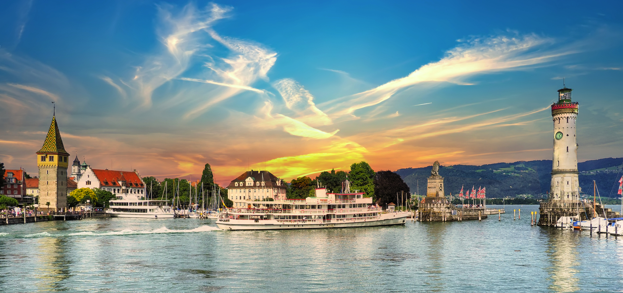 Hafen von Lindau am Bodensee mit Boot, Leuchtturm und Stadtansicht bei Sonnenuntergang.