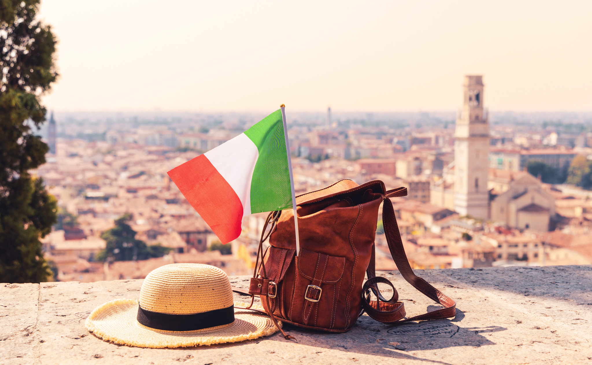 Hut, Rucksack und italienische Flagge vor Stadtpanorama.