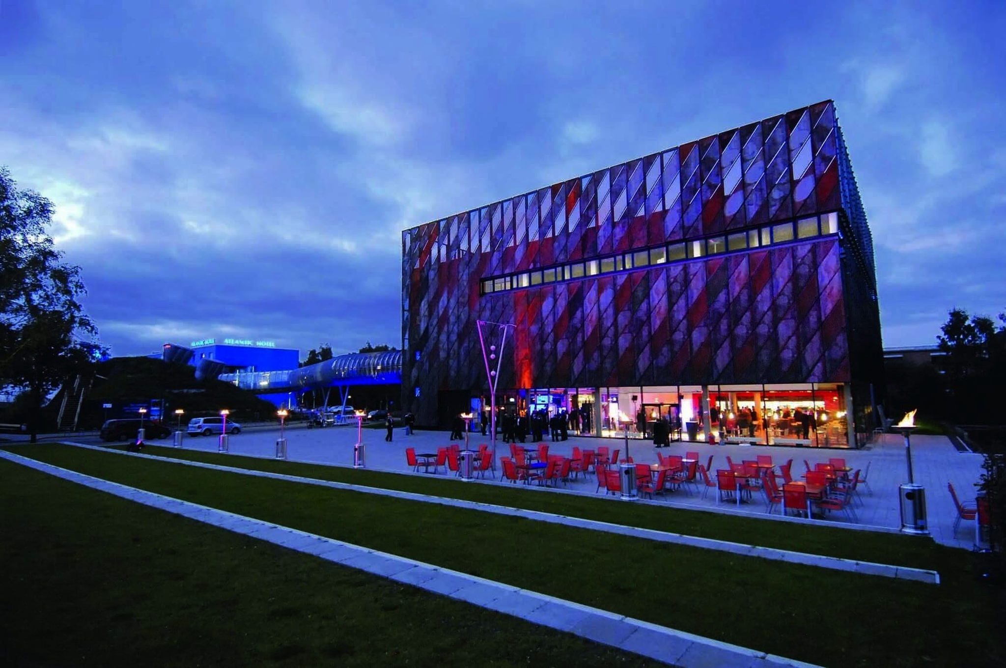 Moderne Gebäudeansicht bei Dämmerung mit beleuchteter Fläche und Café-Terrasse.