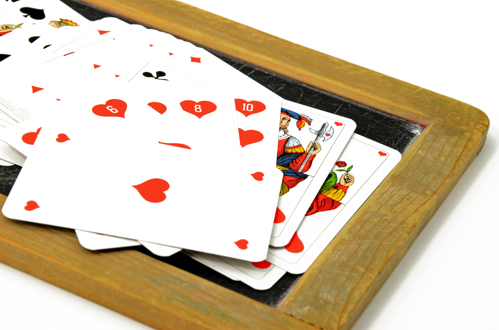 Spielkarten mit Herz-, Pik- und Kreuzsymbolen auf einem schwarzen Brett.