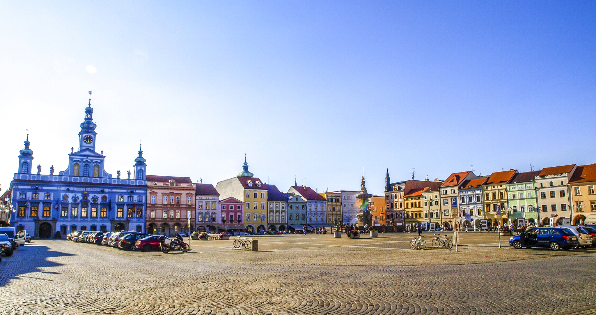 Historischer Platz mit bunten Gebäuden und einem Brunnen an einem sonnigen Tag.
