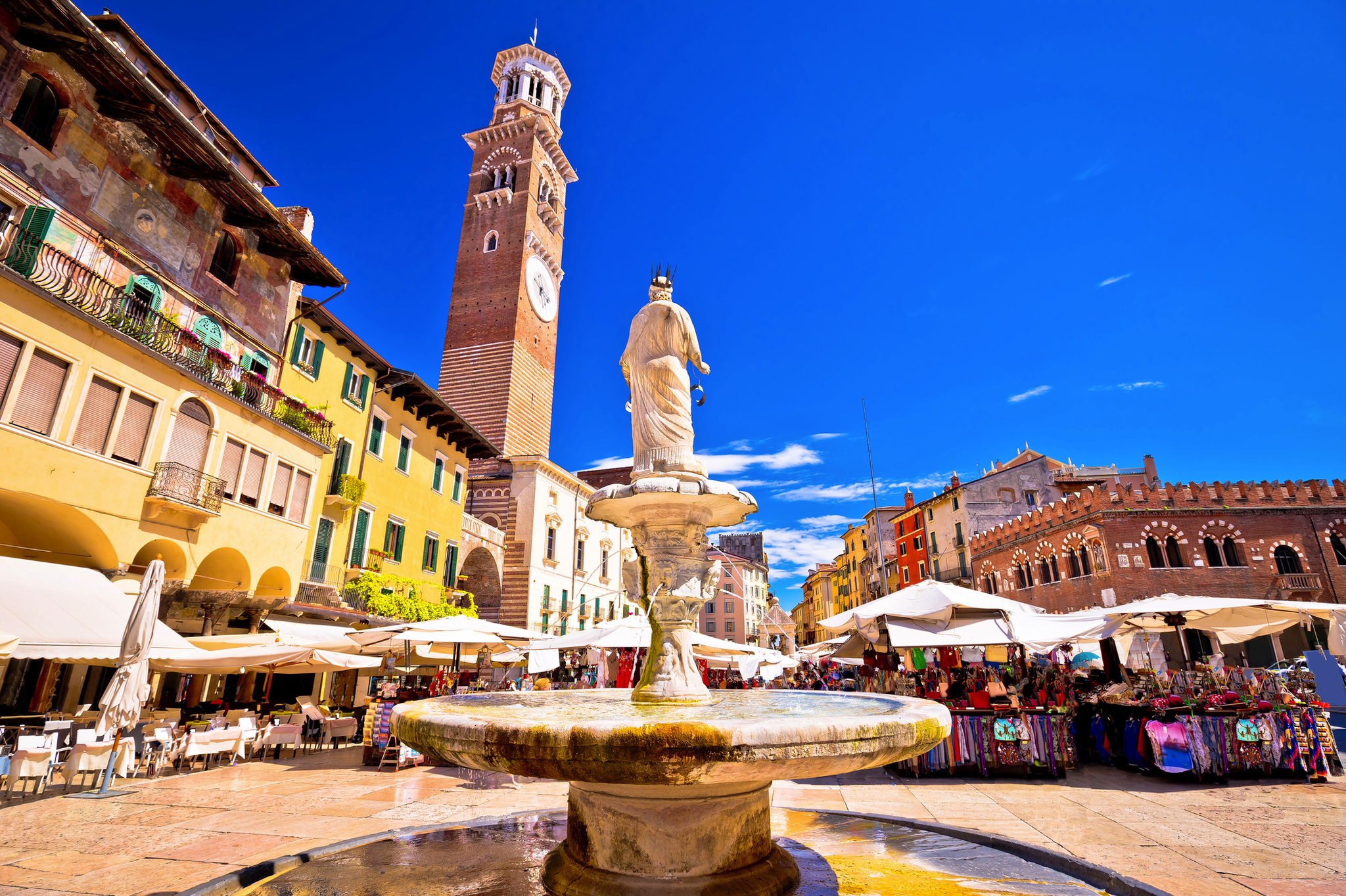 Marktplatz mit Brunnen und Uhrturm an einem sonnigen Tag in einer europäischen Stadt.