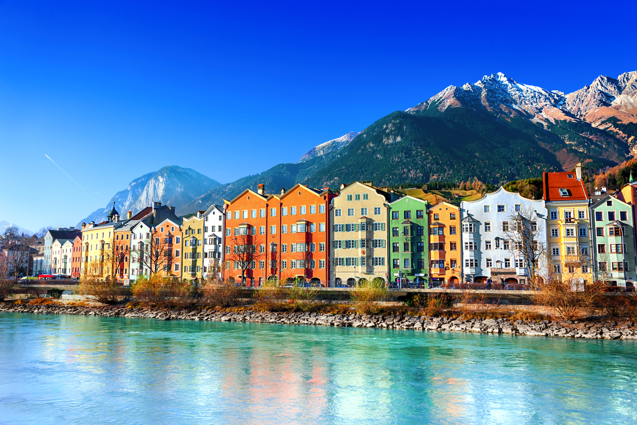 Bunte Häuserreihe am Fluss vor Bergkulisse.