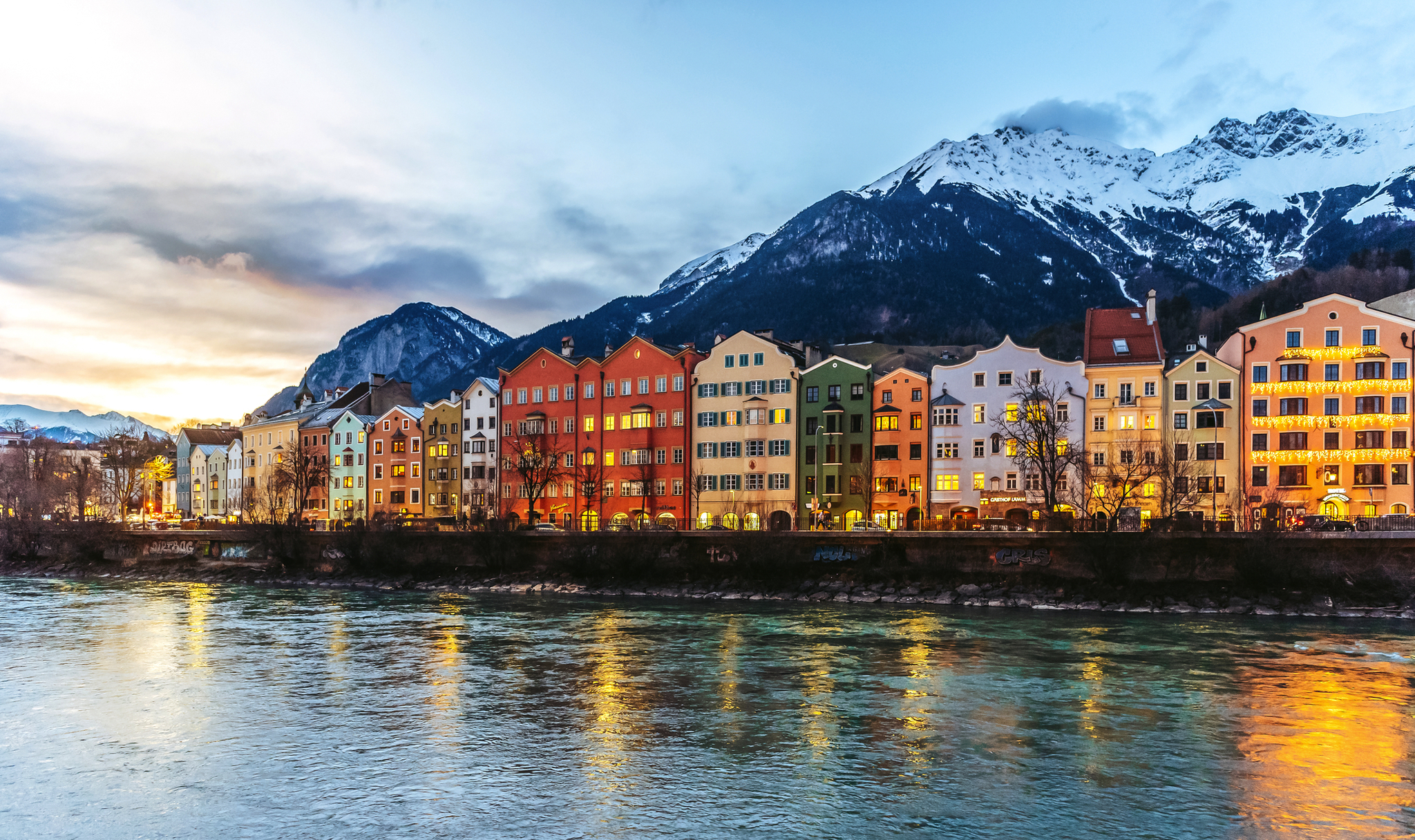 Innsbruck im Winter, bunte Häuser am Flussufer vor schneebedeckten Alpen.
