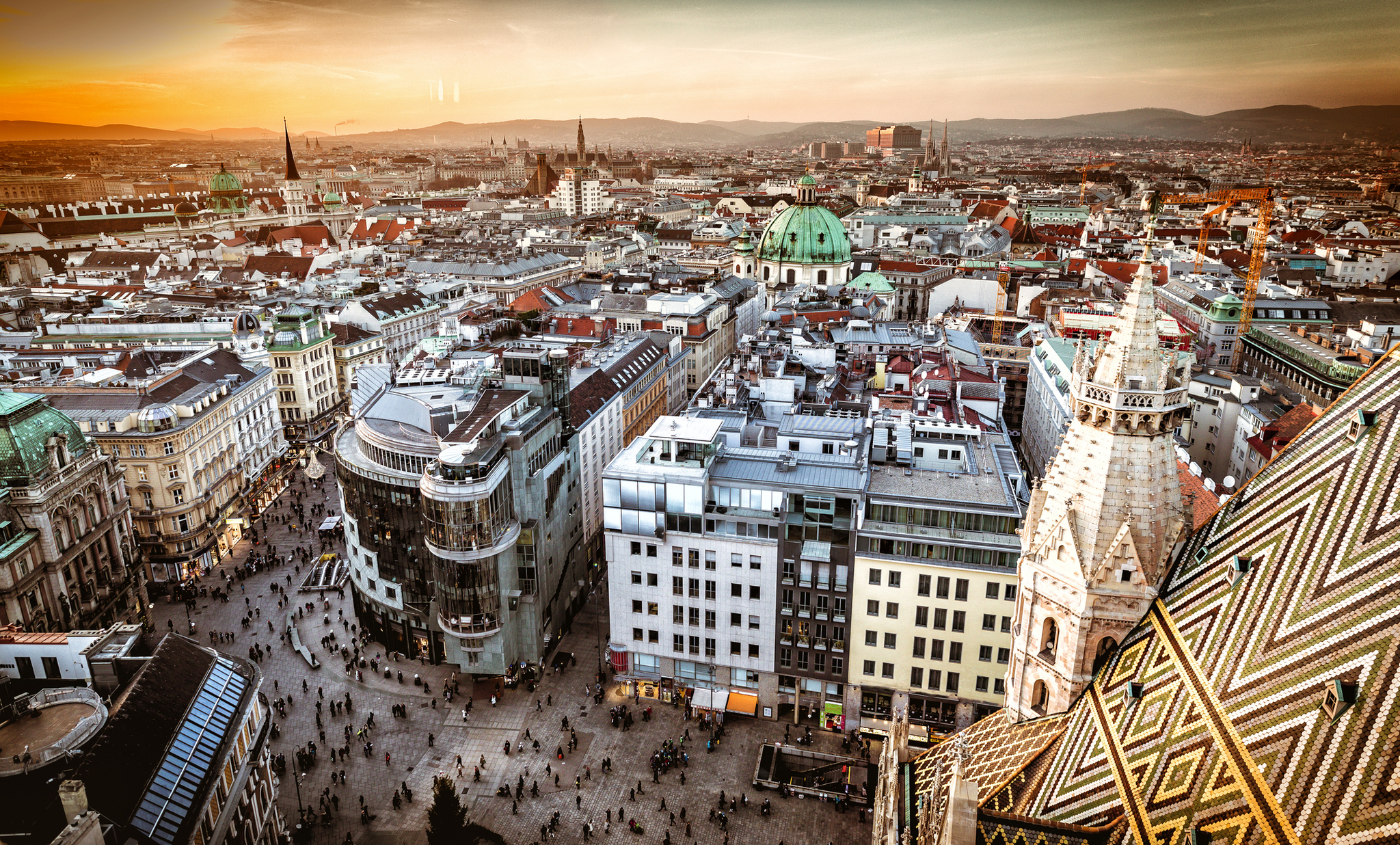 Luftaufnahme von Wien bei Sonnenuntergang, zeigt die Stadtlandschaft mit Gebäuden und Straßen.