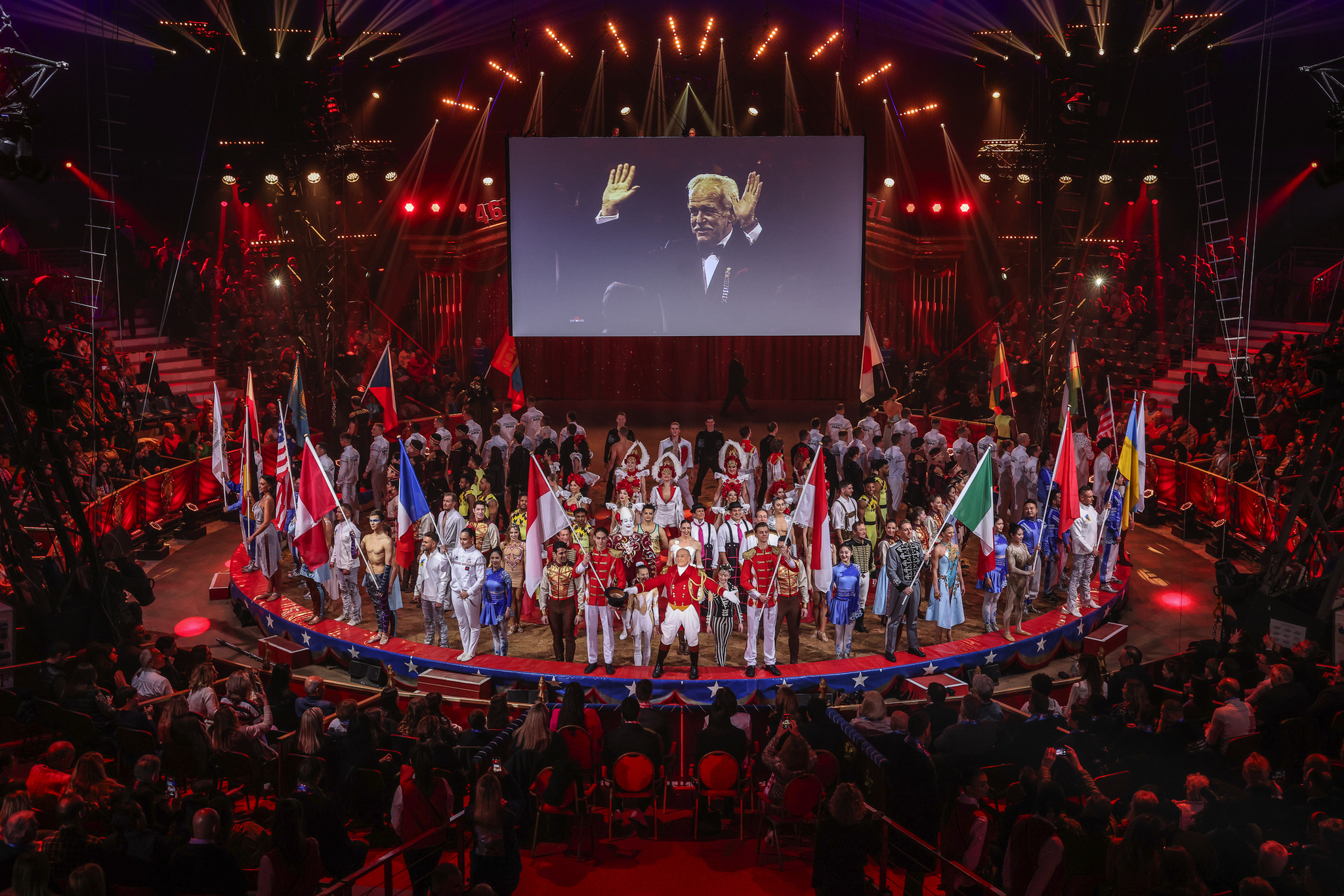 Eine Bühne voller Menschen mit nationalen Flaggen unter einem großen Bildschirm.