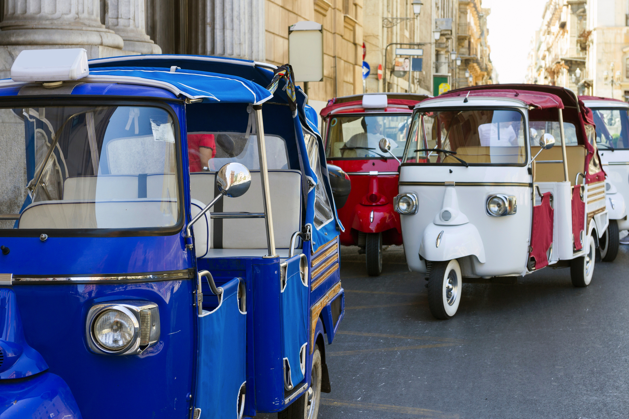 Drei bunte Tuk-Tuks fahren auf einer Stadtstraße.