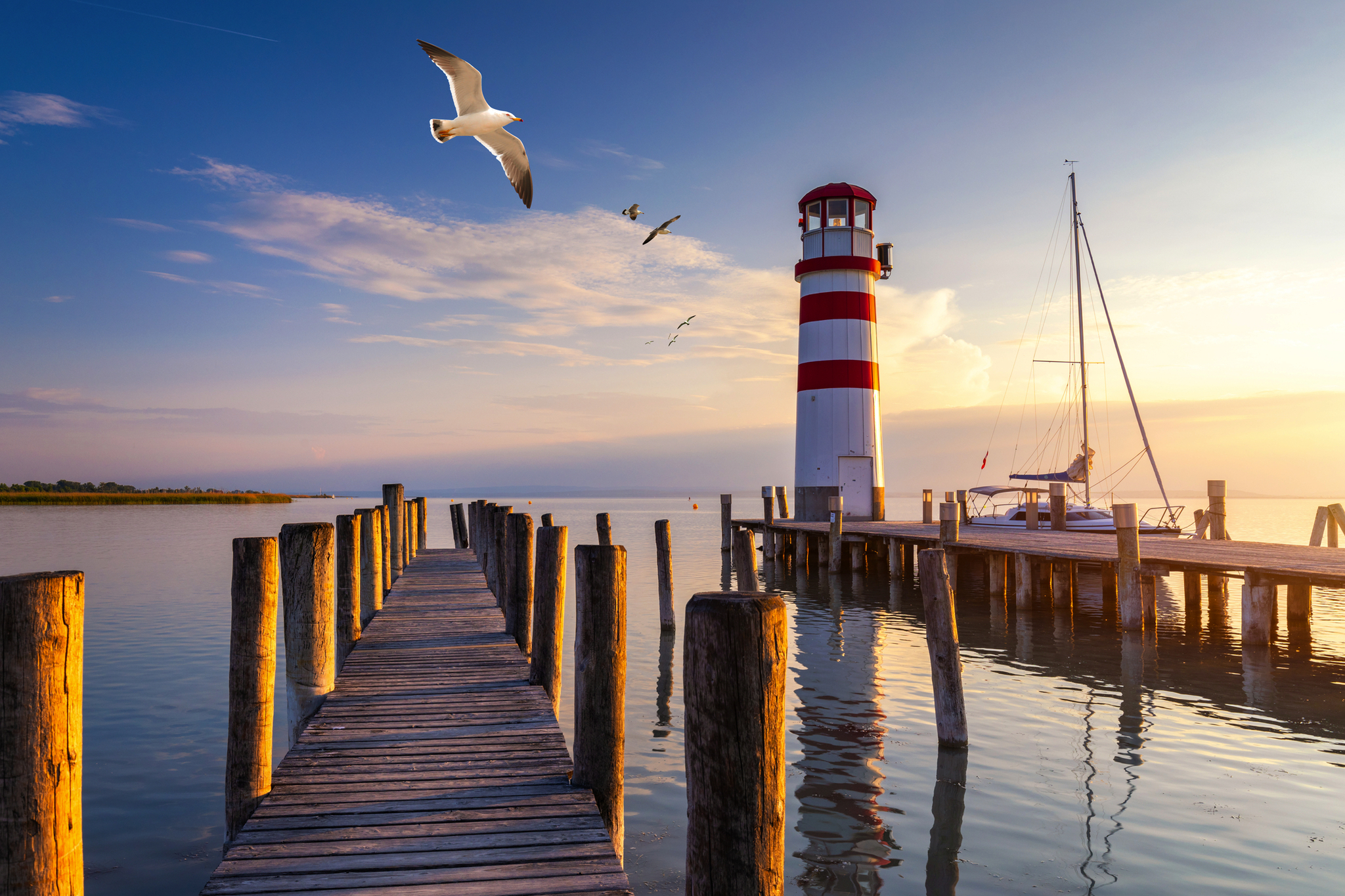 Steg und Leuchtturm am Wasser bei Sonnenuntergang mit Möwen im Himmel