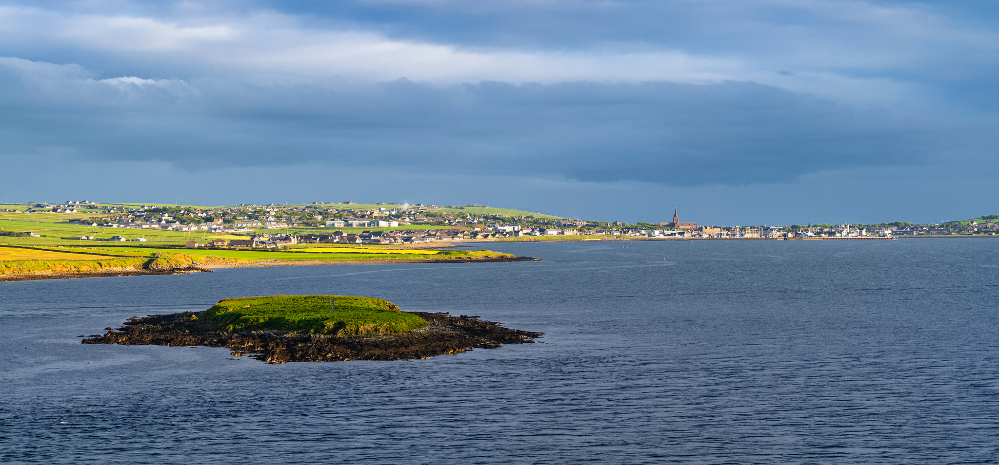 Insel im Meer mit Stadt im Hintergrund bei bewölktem Himmel