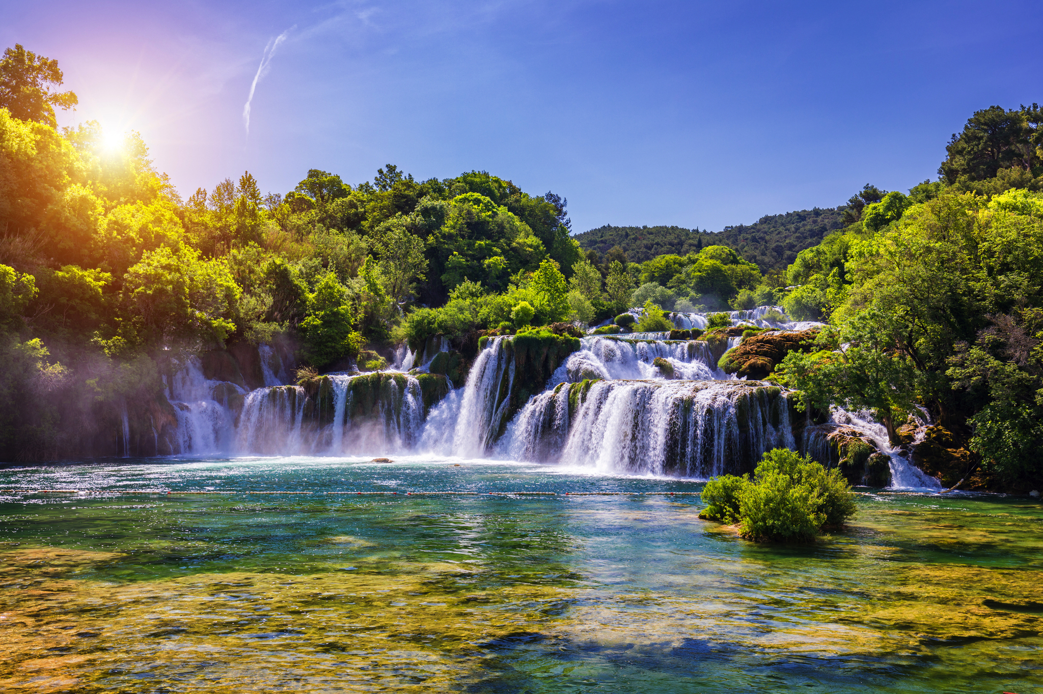 Wasserfall inmitten grüner Wälder und blauem Himmel bei Sonnenschein