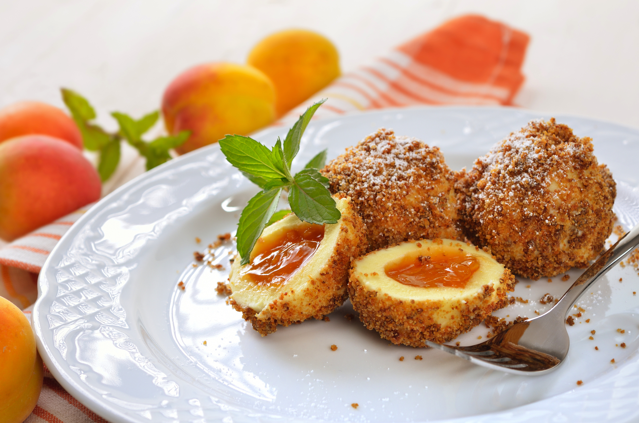 Drei Aprikosenknödel auf einem weißen Teller mit Minzblattgarnitur.