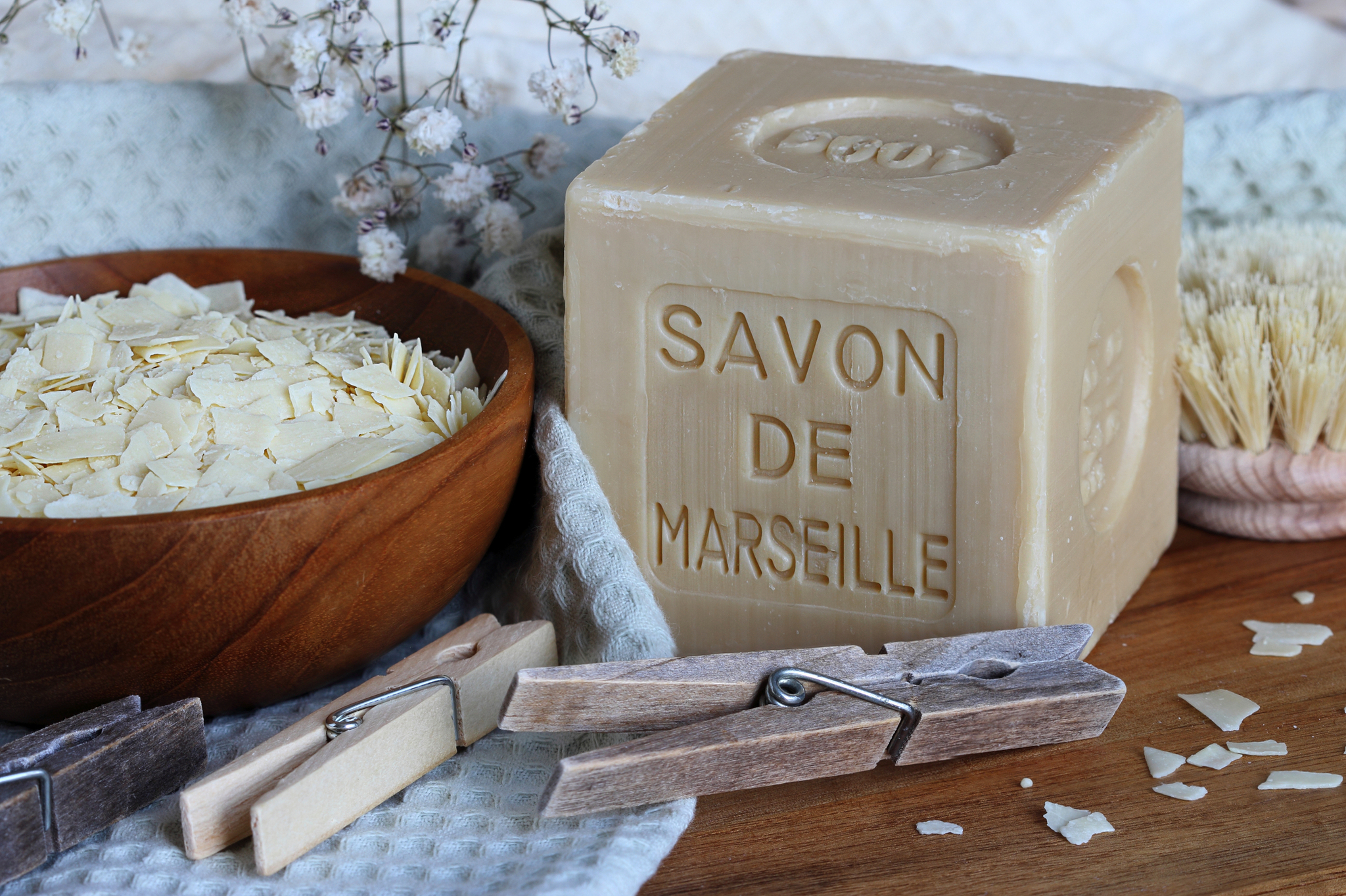 Seifenstück mit Gravur "Savon de Marseille" neben Schüssel mit Seifenflocken.