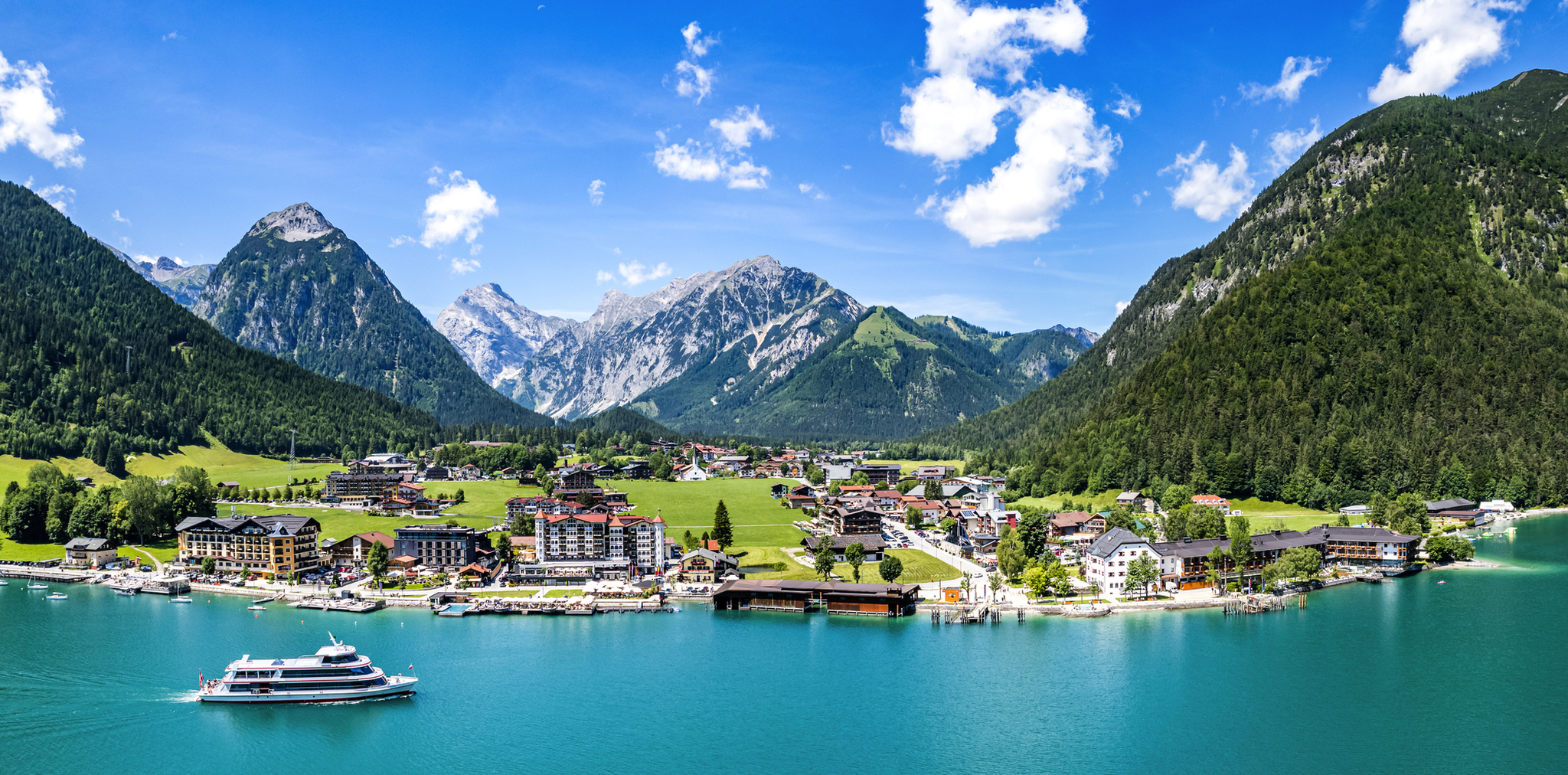 Szenische Ansicht eines Sees mit Bergen, Dorf und einem Boot bei klarem Himmel.