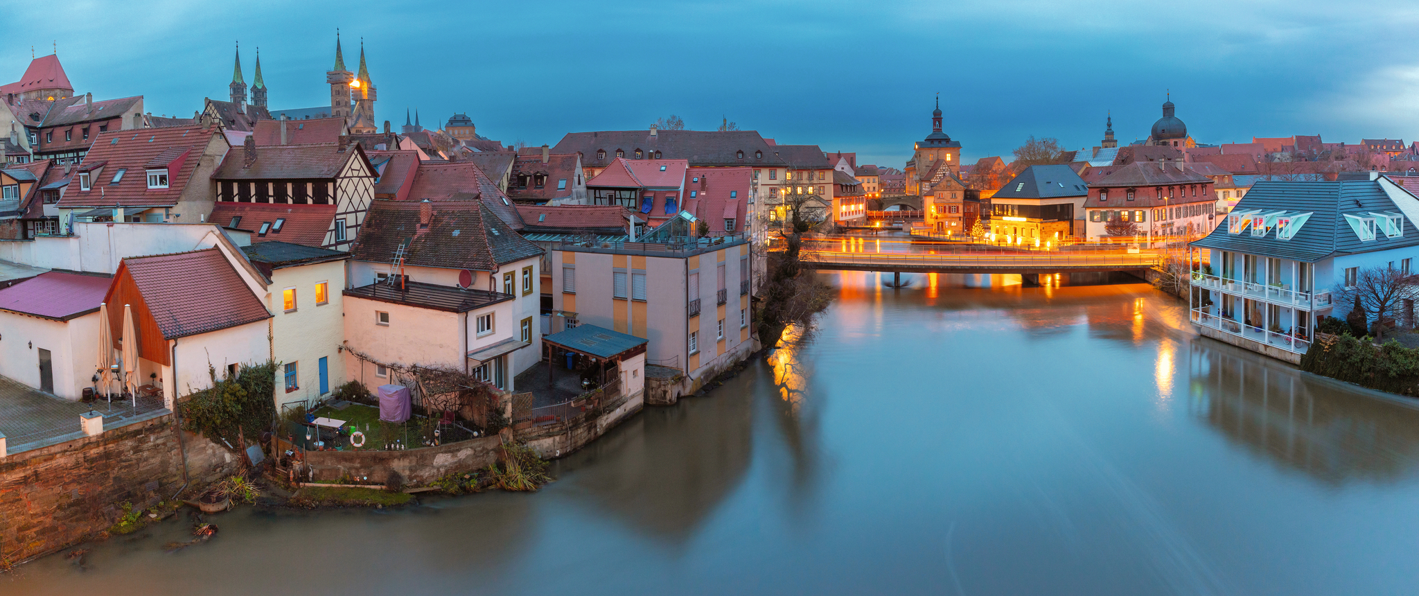 Stadtansicht mit Fluss und beleuchteten Gebäuden in der Abenddämmerung.