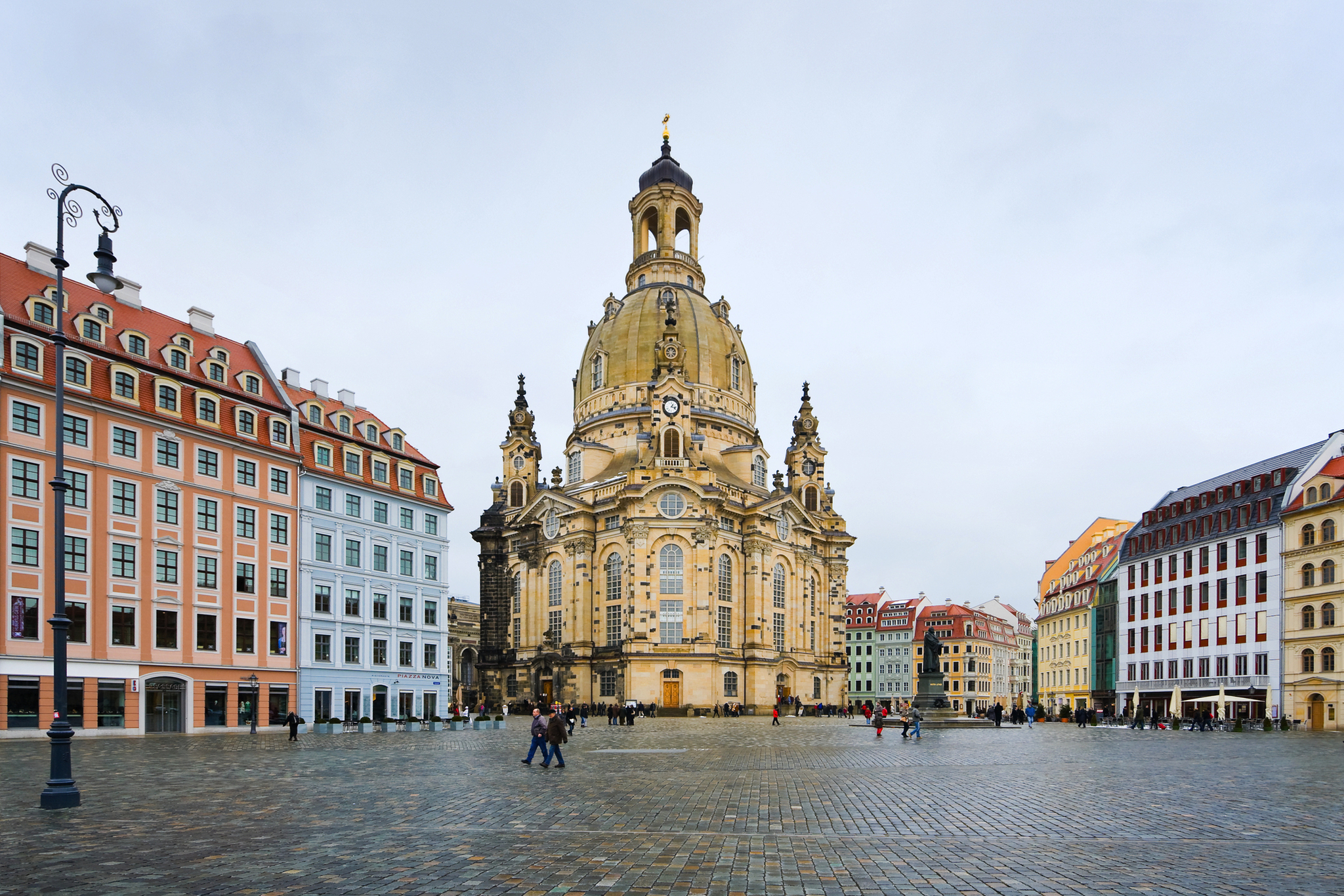 Barocke Kirche auf einem historischen Platz mit umliegenden Gebäuden und wenigen Menschen.