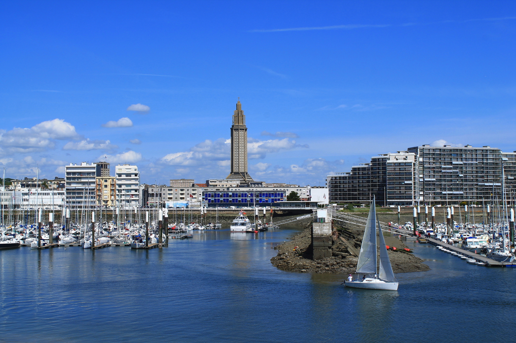 Hafen mit Segelboot, Gebäuden und Turm unter blauem Himmel.