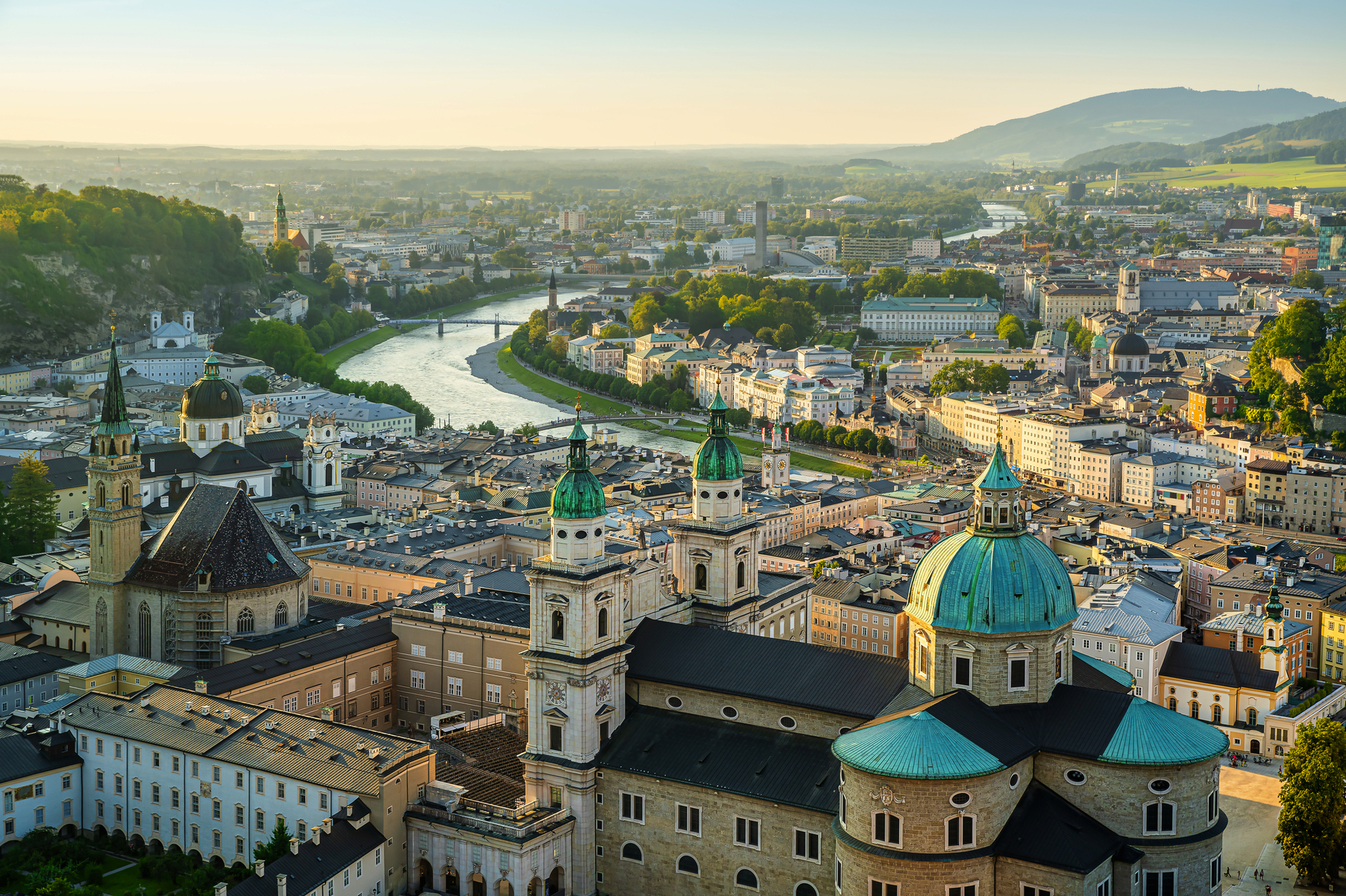 Stadtansicht von Salzburg mit Fluss und historischen Gebäuden im Abendlicht.