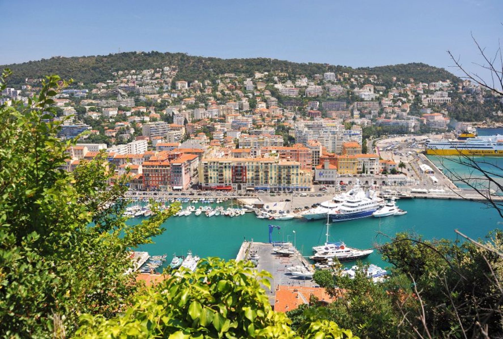Hafenstadt mit vielen Gebäuden und Booten, umgeben von grünen Hügeln.