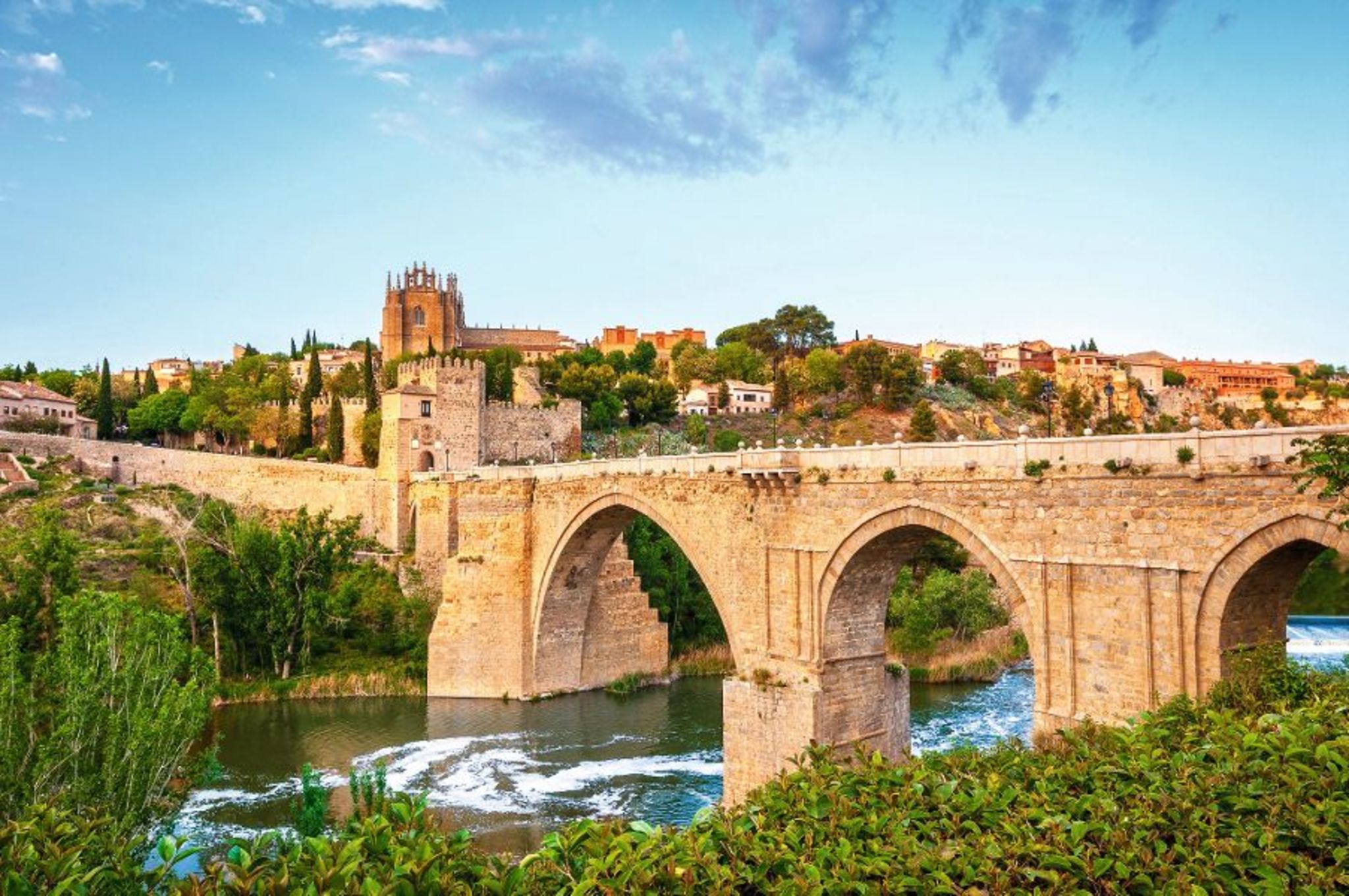 Steinbrücke über einen Fluss mit historischer Architektur im Hintergrund.