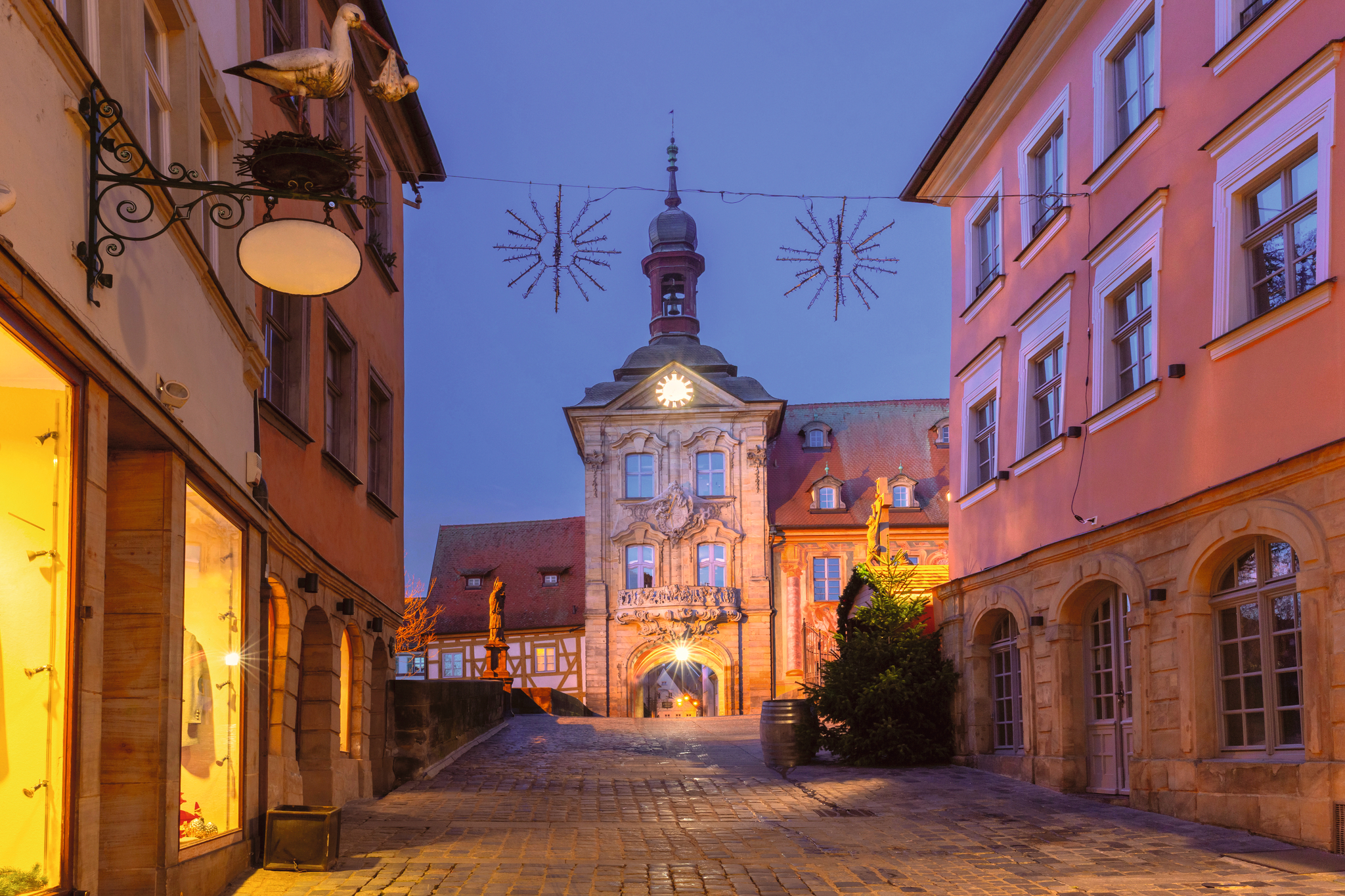 Straße mit historischen Gebäuden und beleuchtetem Rathaus bei Dämmerung