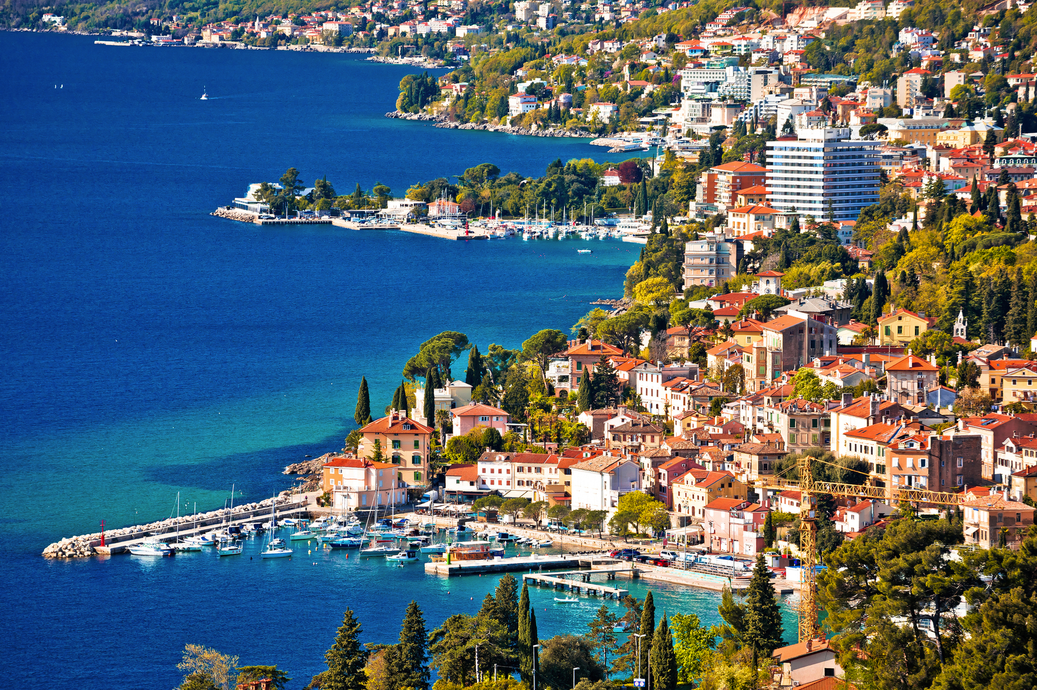 Küstenstadt mit Hafen und vielen Gebäuden am türkisfarbenen Meer.