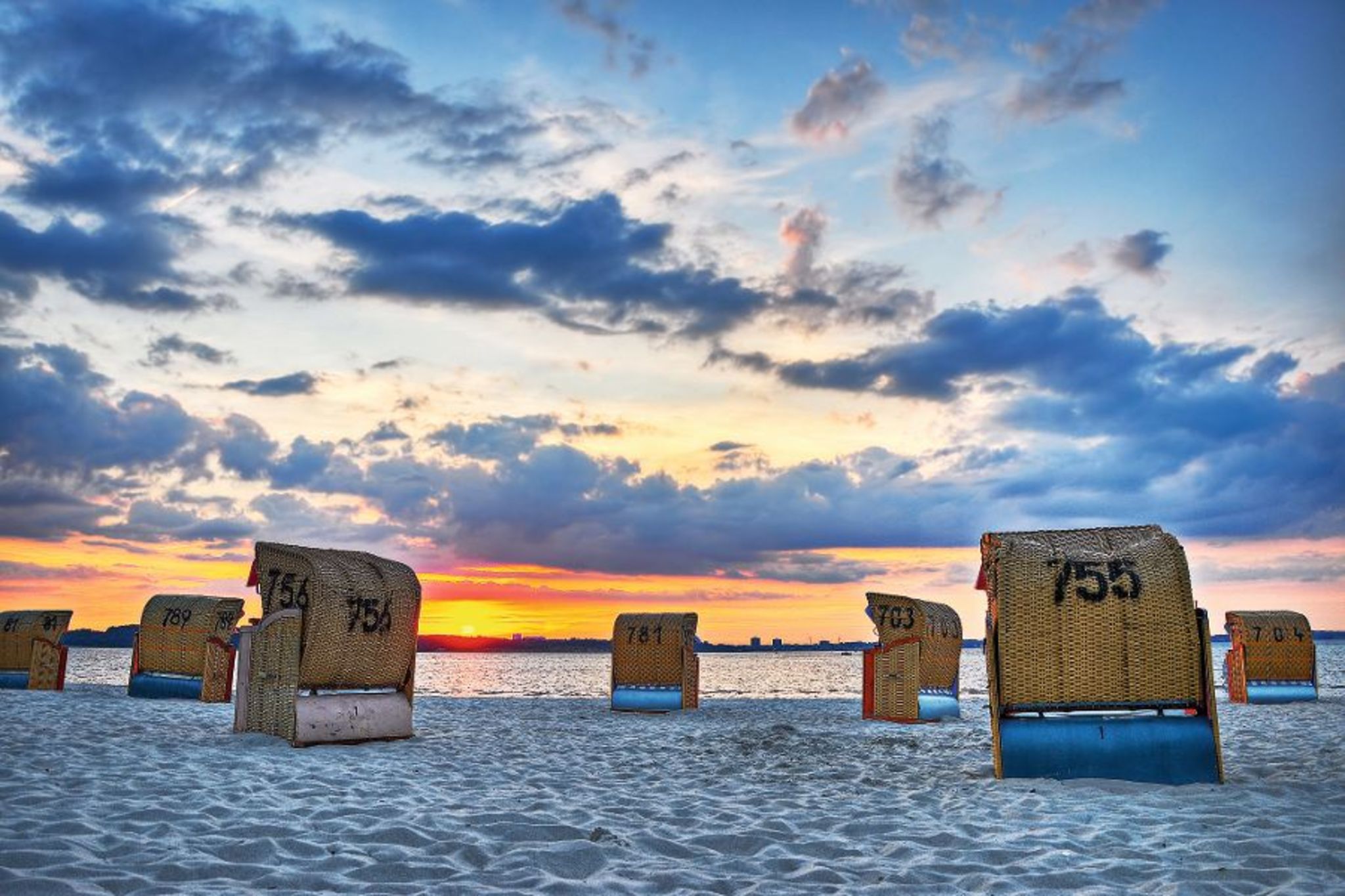 Strandkörbe am Sandstrand bei Sonnenuntergang mit Wolken am Himmel.