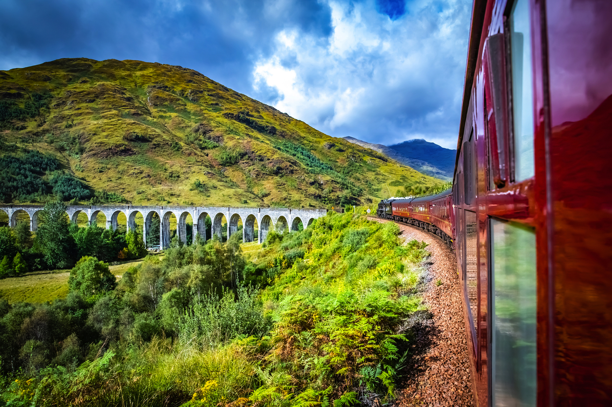Zug fährt über ein Viadukt in grüner Hügellandschaft.